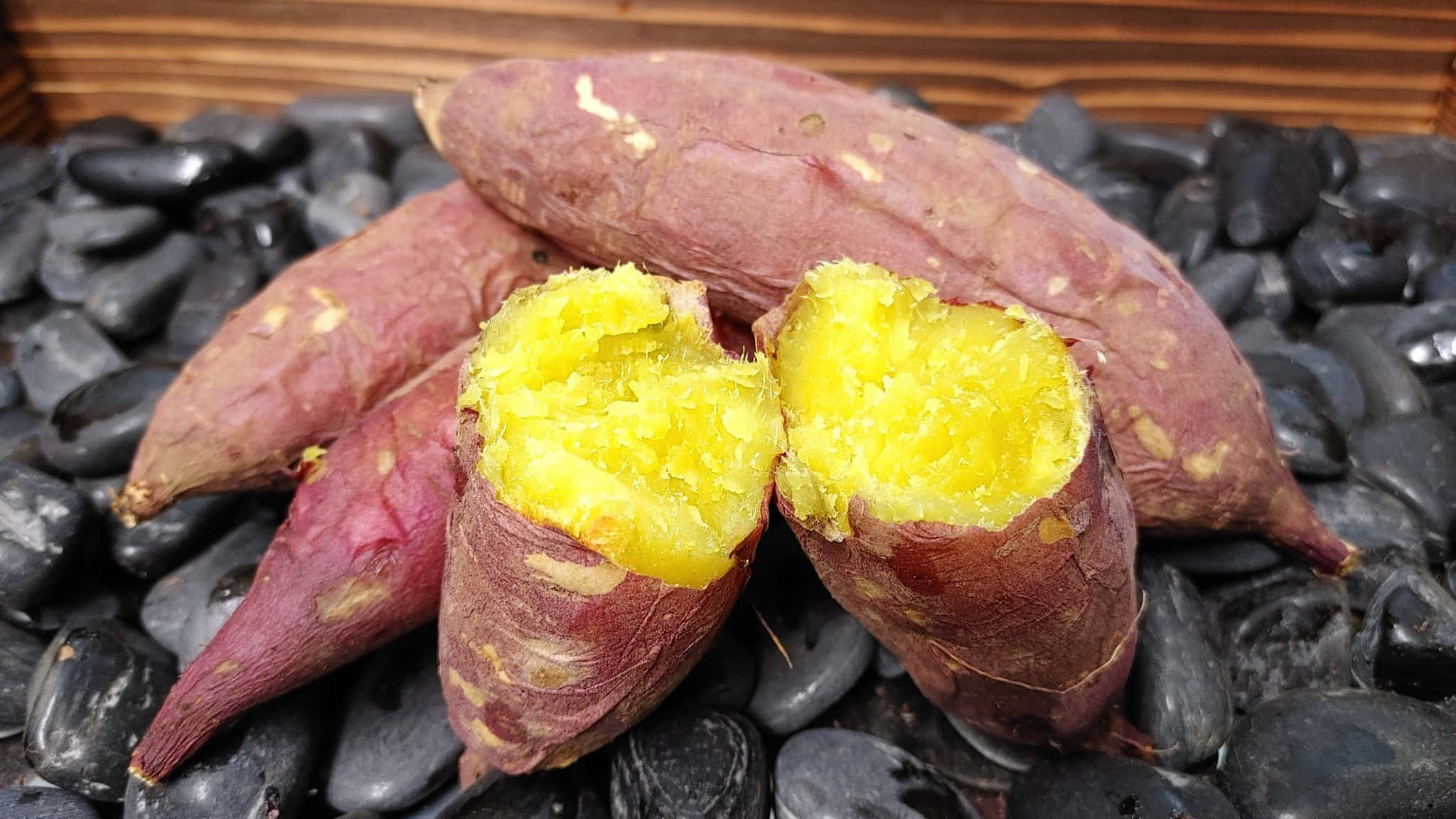 Yellow Sweet Potato 桌布 壁紙 — 新鮮烤製的番薯，金黃鬆軟的內部躺在光滑的黑色河石床上。