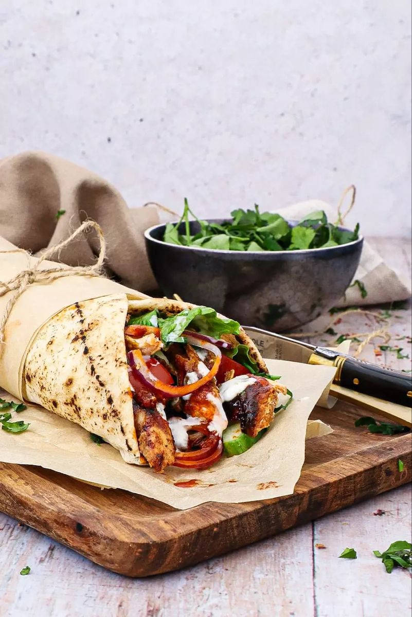 Burrito 桌布 壁紙 — 新鮮烤雞肉捲，充滿色彩繽紛的蔬菜和奶油醬汁，放在質樸的木板上，旁邊有一碗青菜。