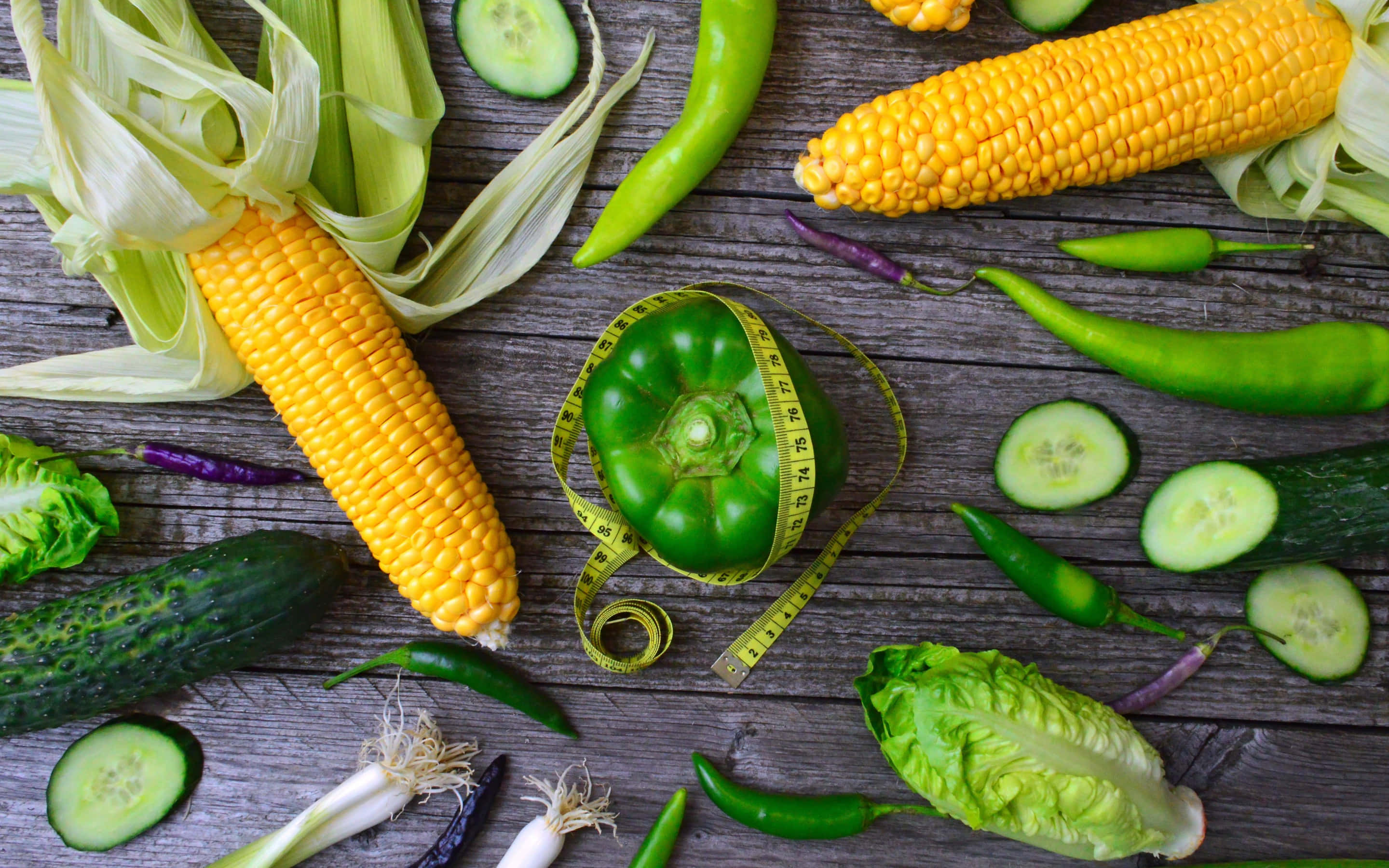 Corn 桌布 壁紙 — 新鮮玉米、小黃瓜和甜椒擺放在經風化的木頭上，綠色甜椒上纏繞著軟尺。