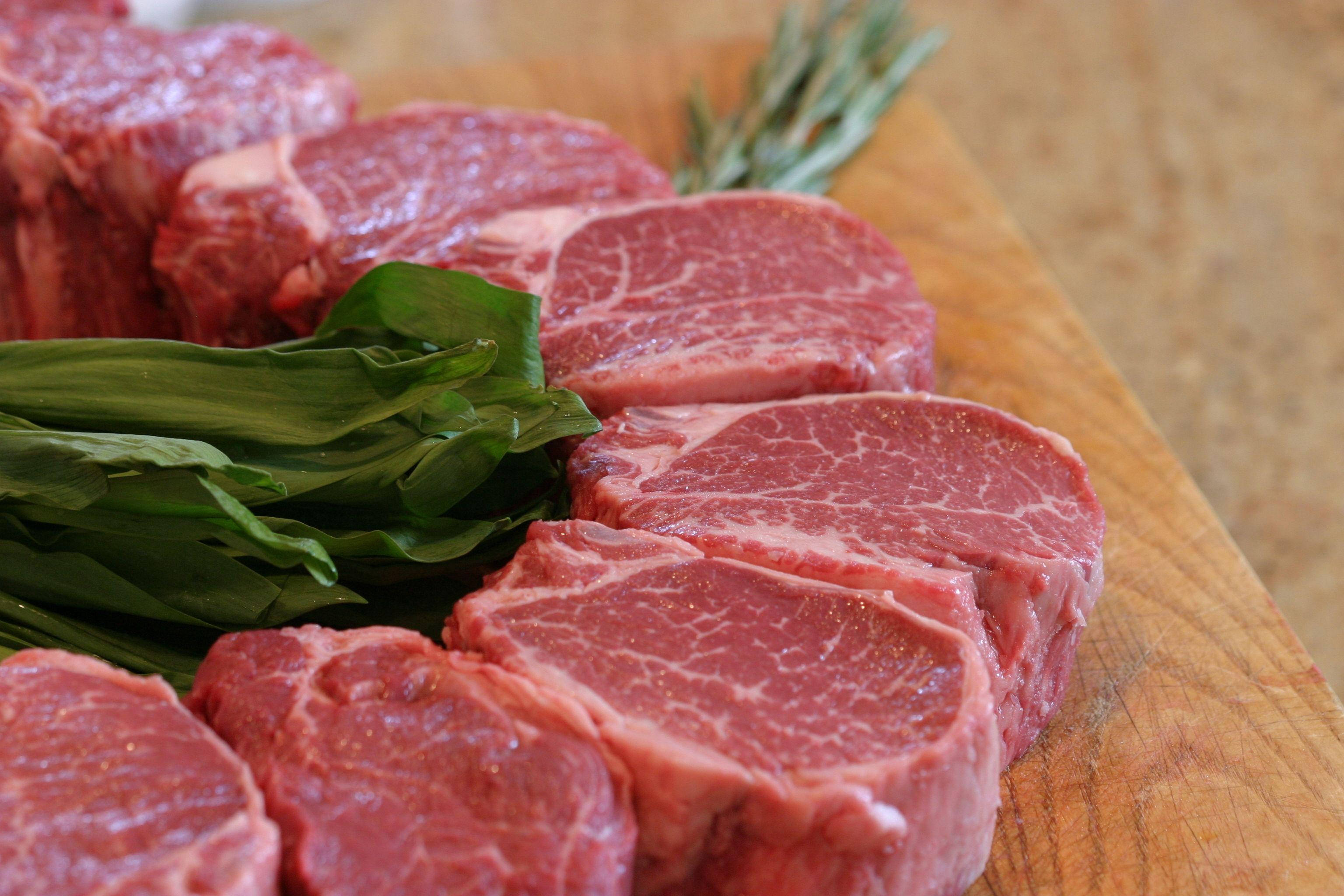meat 桌布 壁紙 — 新鮮生牛肉排搭配綠色香草，擺放在木製砧板上。