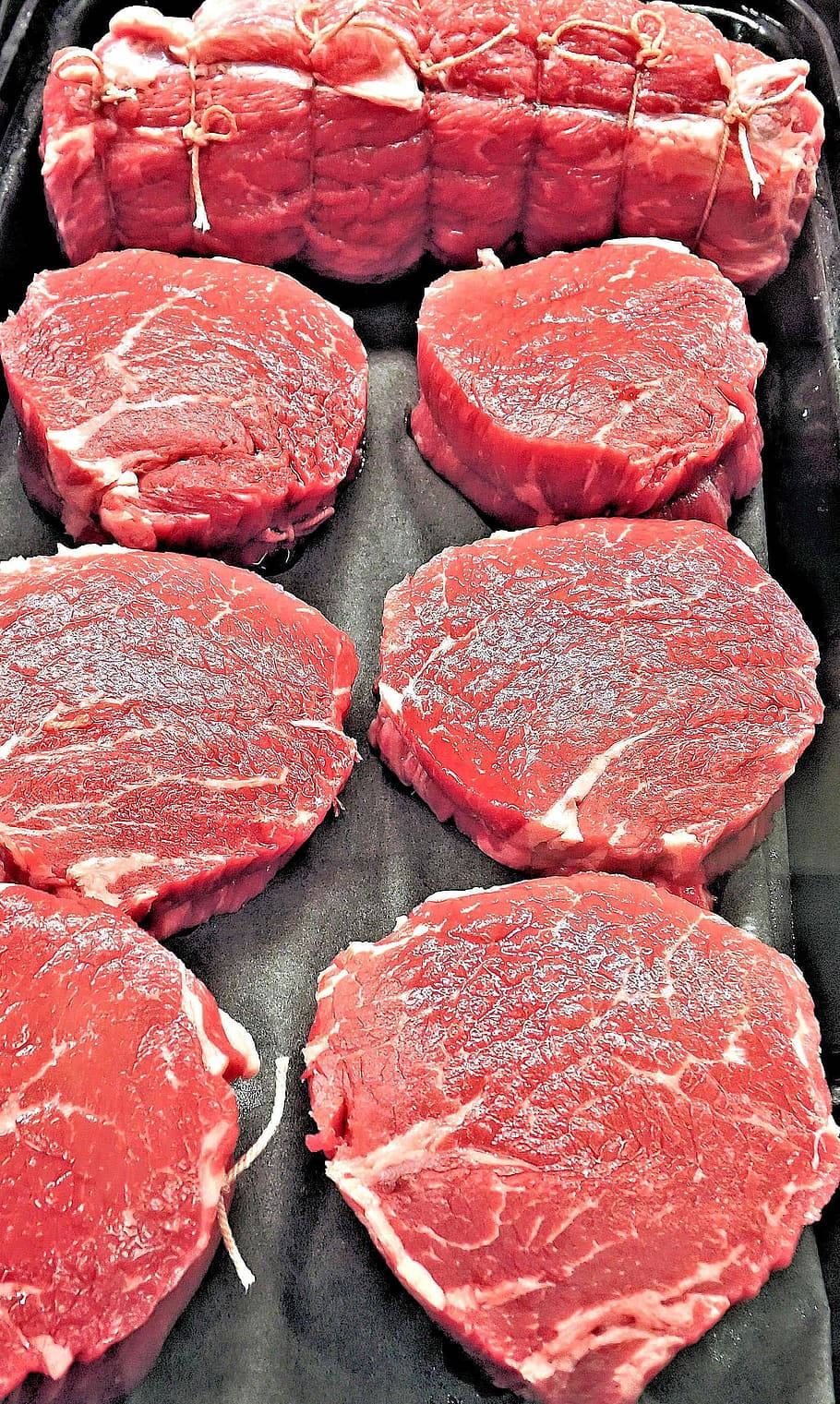 meat 桌布 壁紙 — 新鮮生牛肉牛排和紮好的烤肉整齊排列在深色托盤上，可見大理石紋和光澤表面。