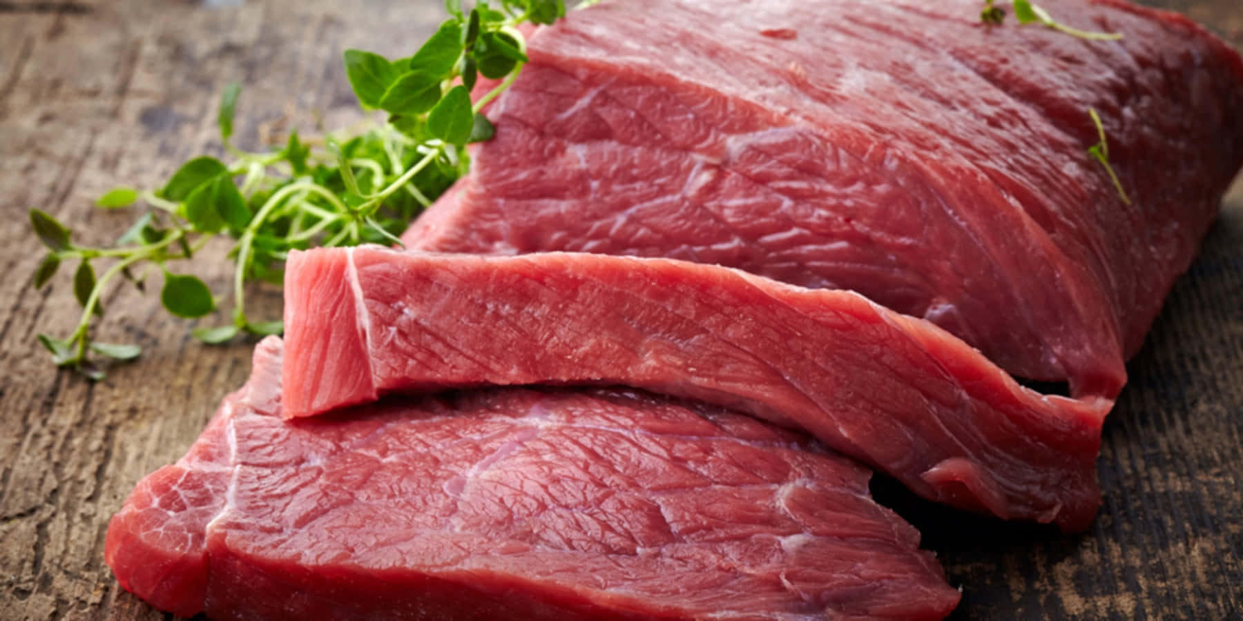 meat 桌布 壁紙 — 新鮮生牛肉牛排搭配香草，放置在質樸的木質表面上，展現豐富的紅色色調和自然質感。