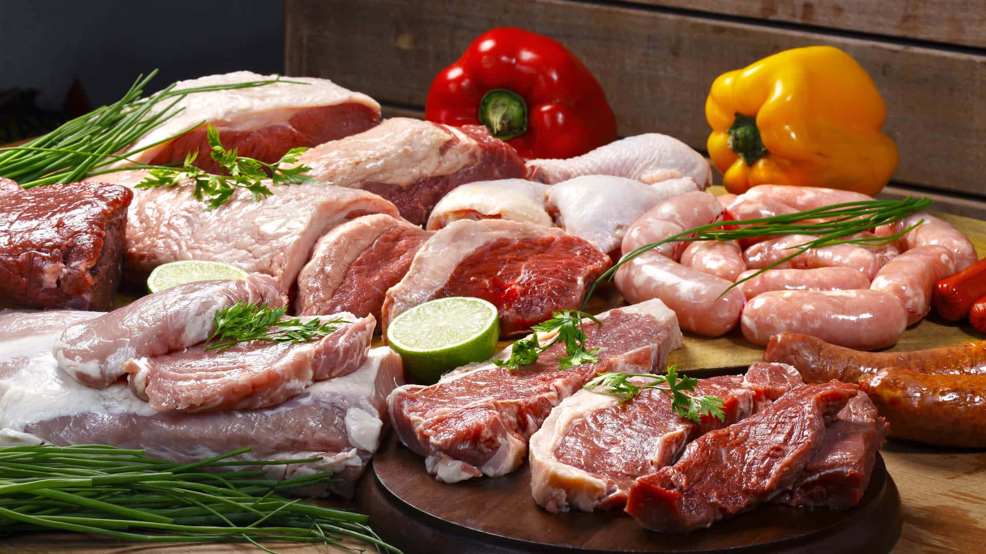meat 桌布 壁紙 — 新鮮生肉包括牛排、香腸和豬排，與萊姆片和彩色甜椒一起擺放在木板上。