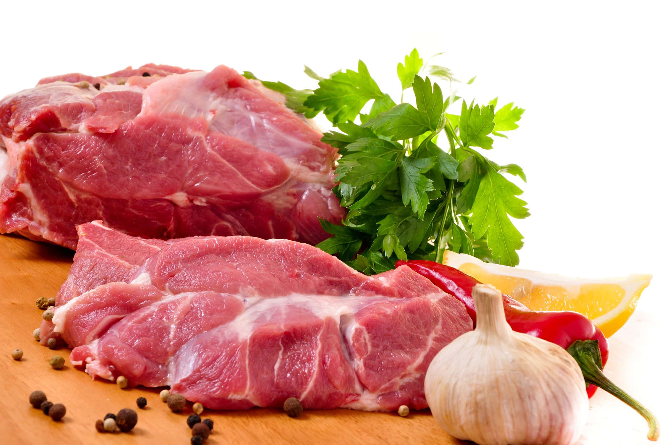 meat 桌布 壁紙 — 新鮮生肉片和整個蒜頭放在木板上，旁邊有歐芹、紅甜椒和胡椒粒。