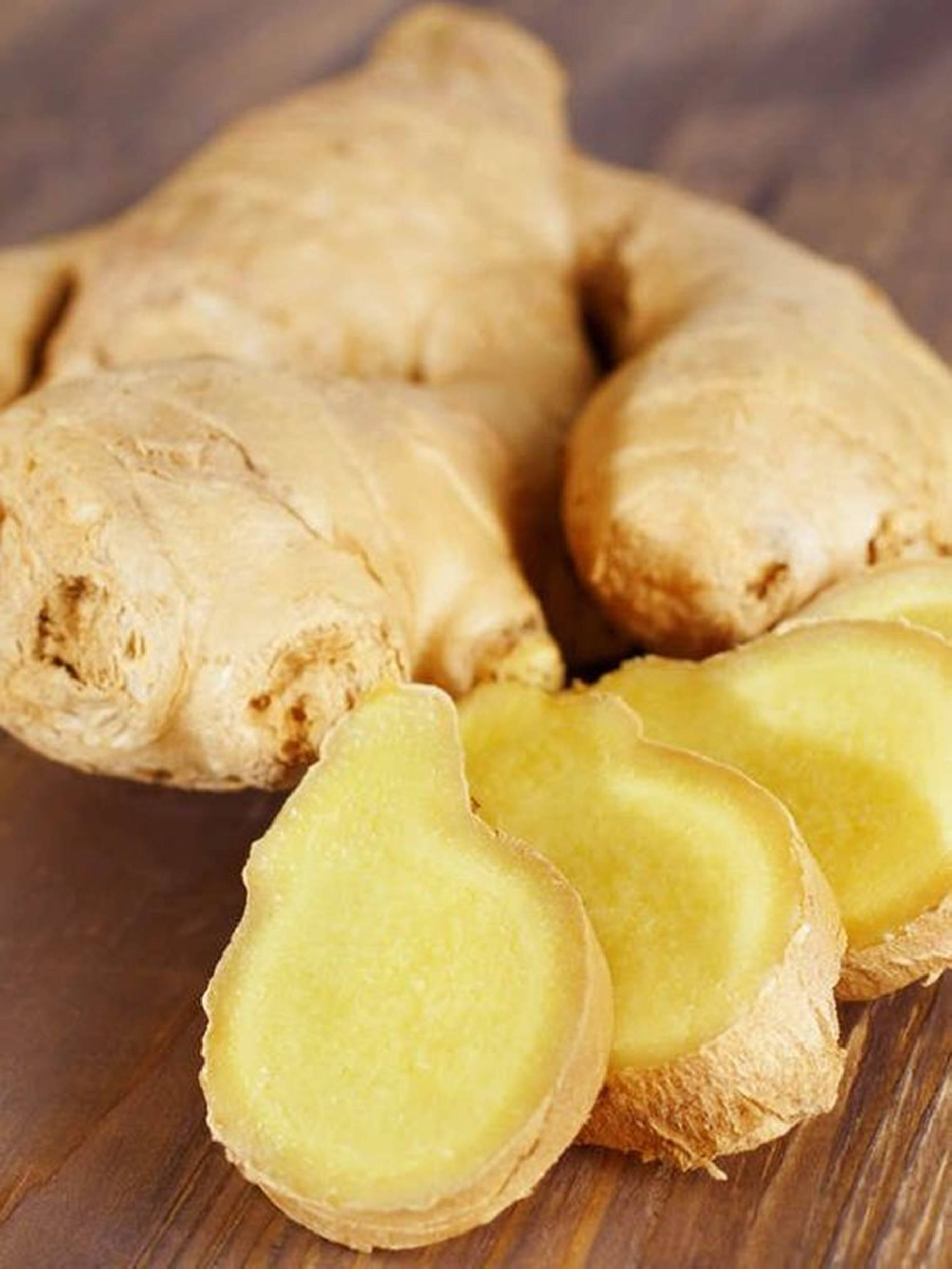 Ginger 桌布 壁紙 — 新鮮生薑根，切片後露出鮮黃色內部，放在質樸的木質表面上。