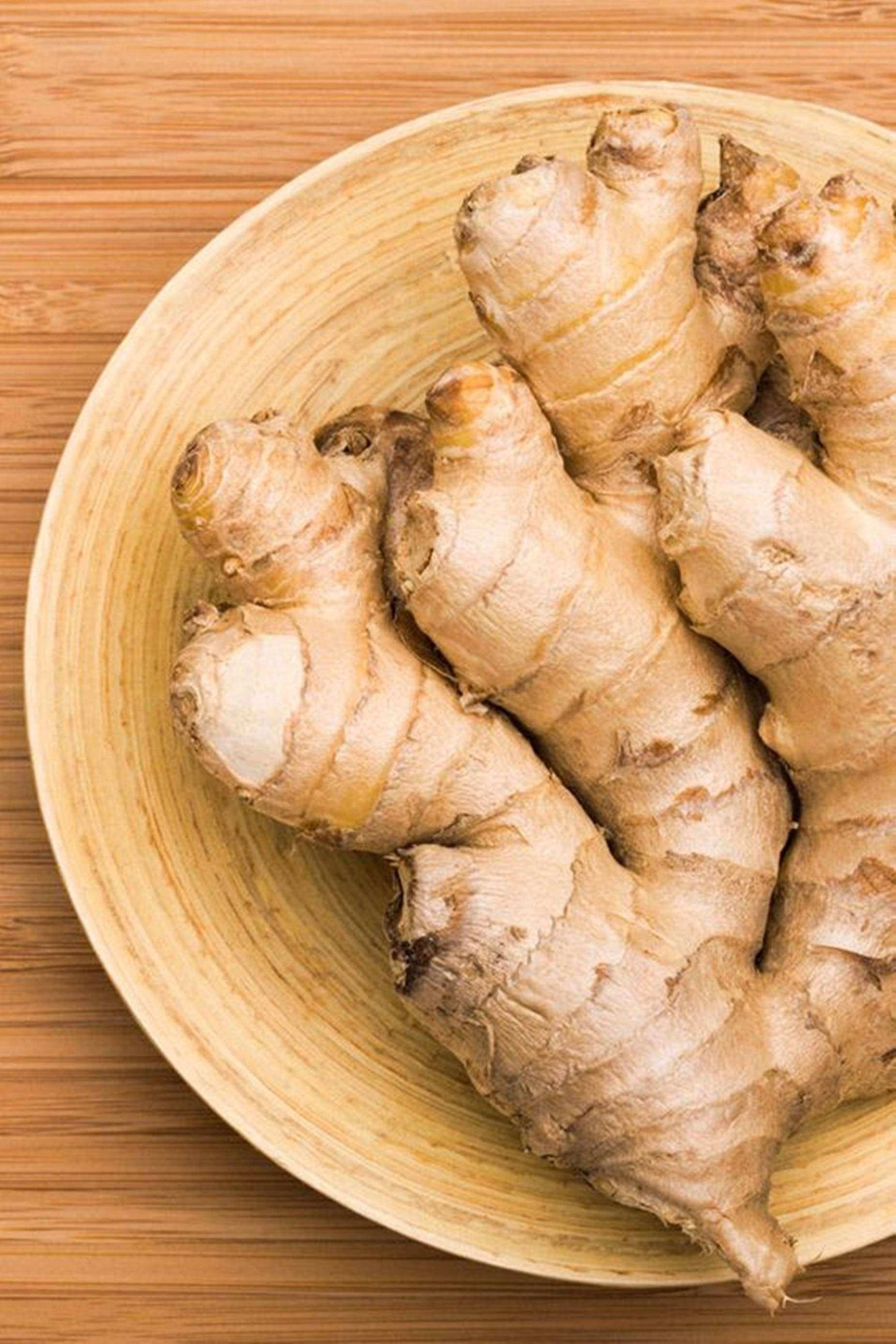 Ginger 桌布 壁紙 — 新鮮生薑根放在一個淺色木碗中，置於帶有天然紋理的竹製表面上。