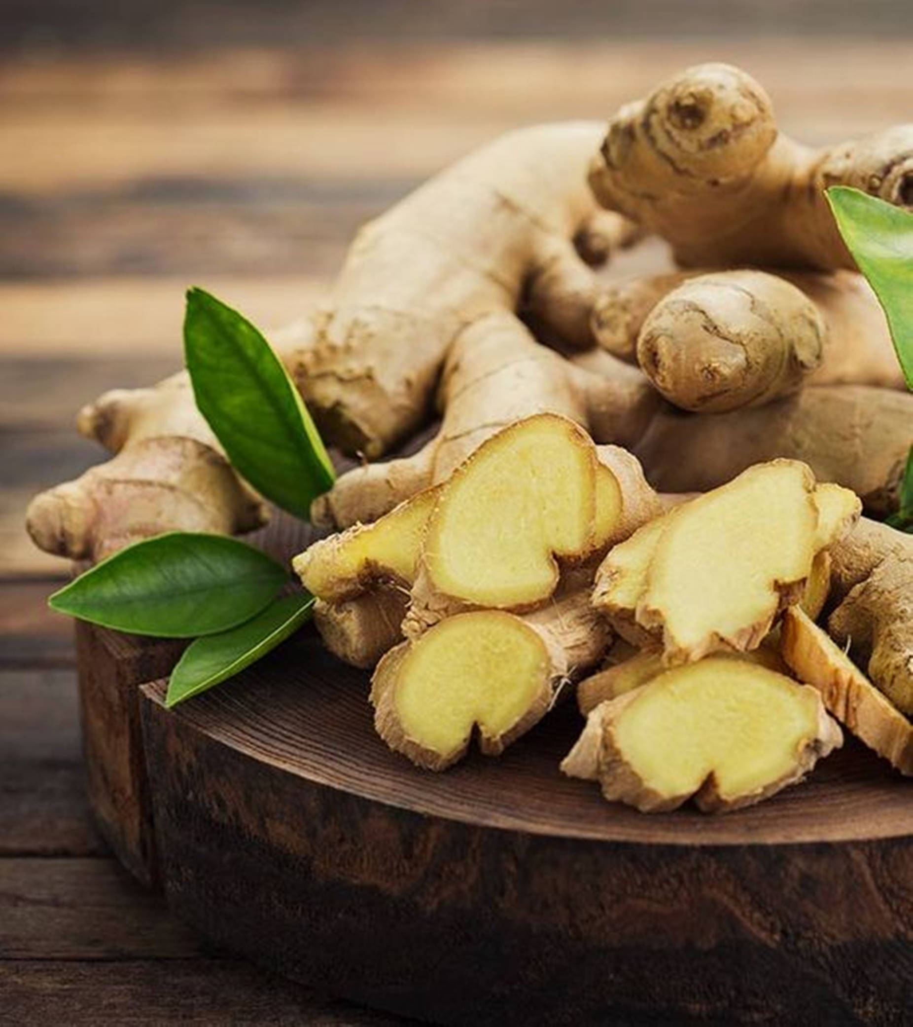 Ginger 桌布 壁紙 — 新鮮生薑根連切片及綠葉，置於質樸木板上。