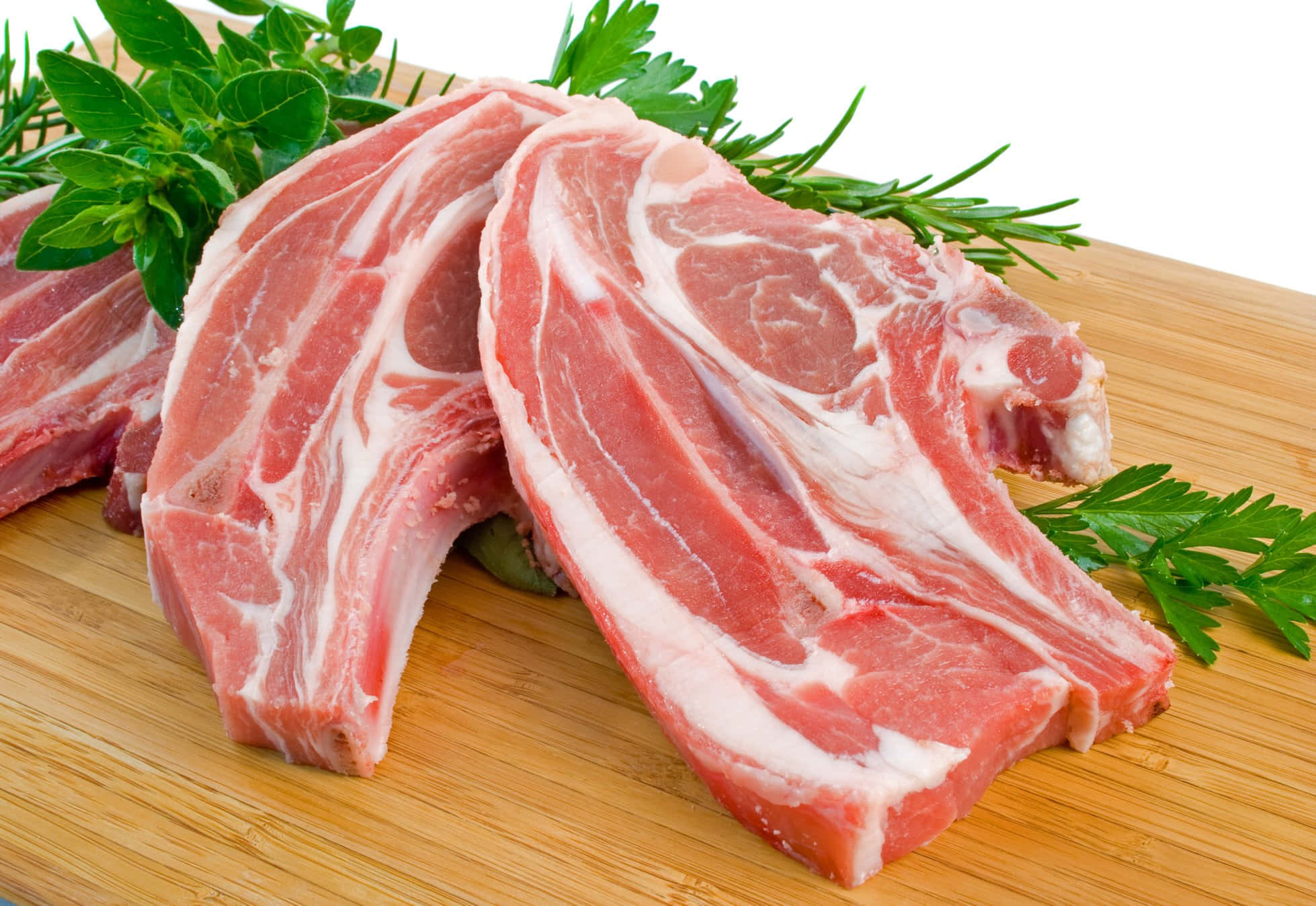 Red Meat 桌布 壁紙 — 新鮮生豬排帶有大理石紋，放在木製砧板上，並以迷迭香和歐芹裝飾。
