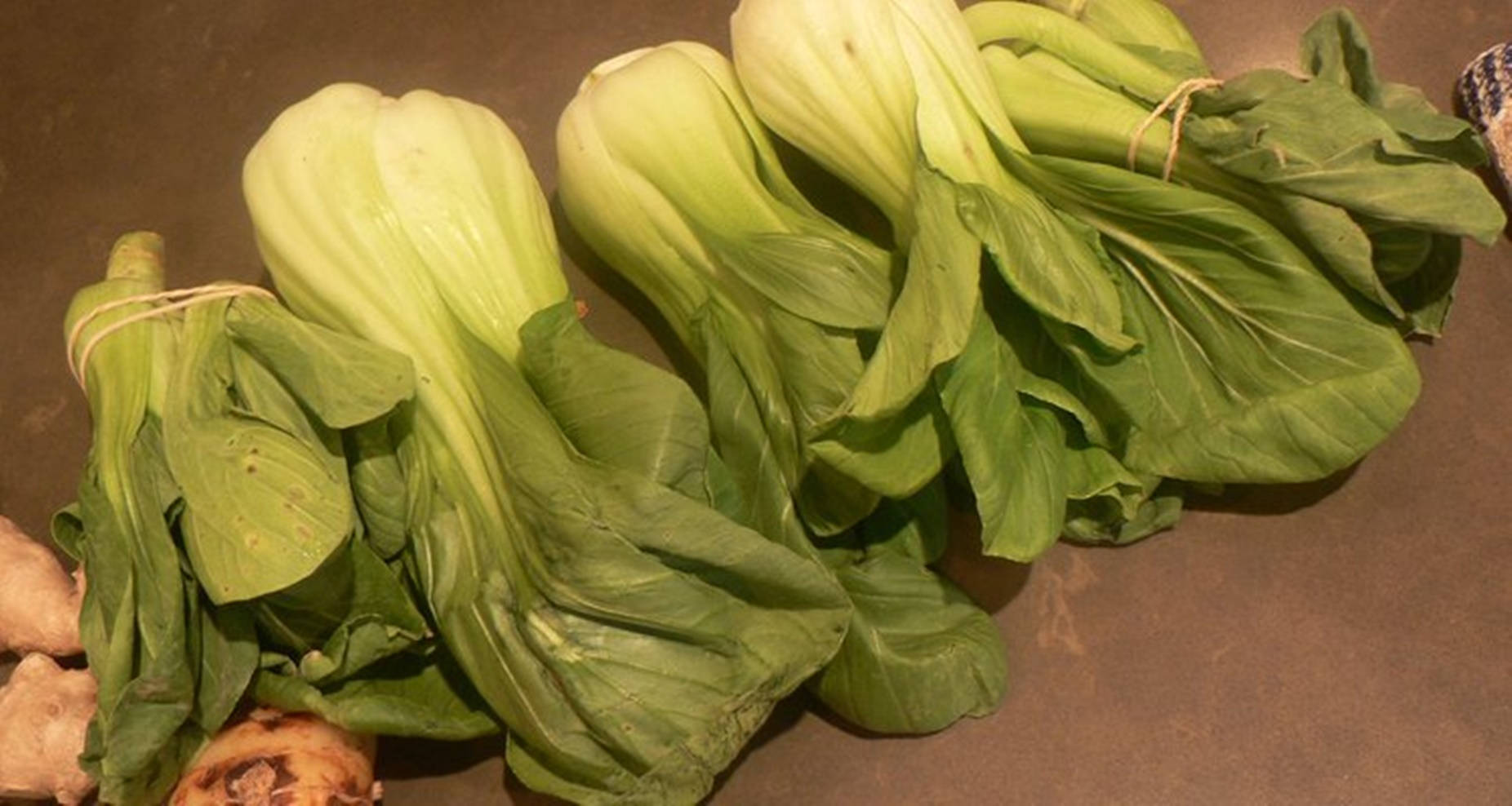 Vegetables 桌布 壁紙 — 新鮮的小白菜束用麻繩捆綁，放在深色檯面上，旁邊有薑根。