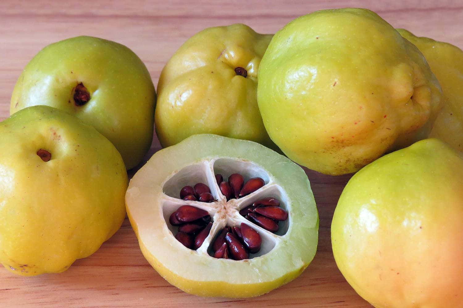 Quince 桌布 壁紙 — 新鮮的榲桲果實，其中一個切開露出紅色種子在木質表面上。