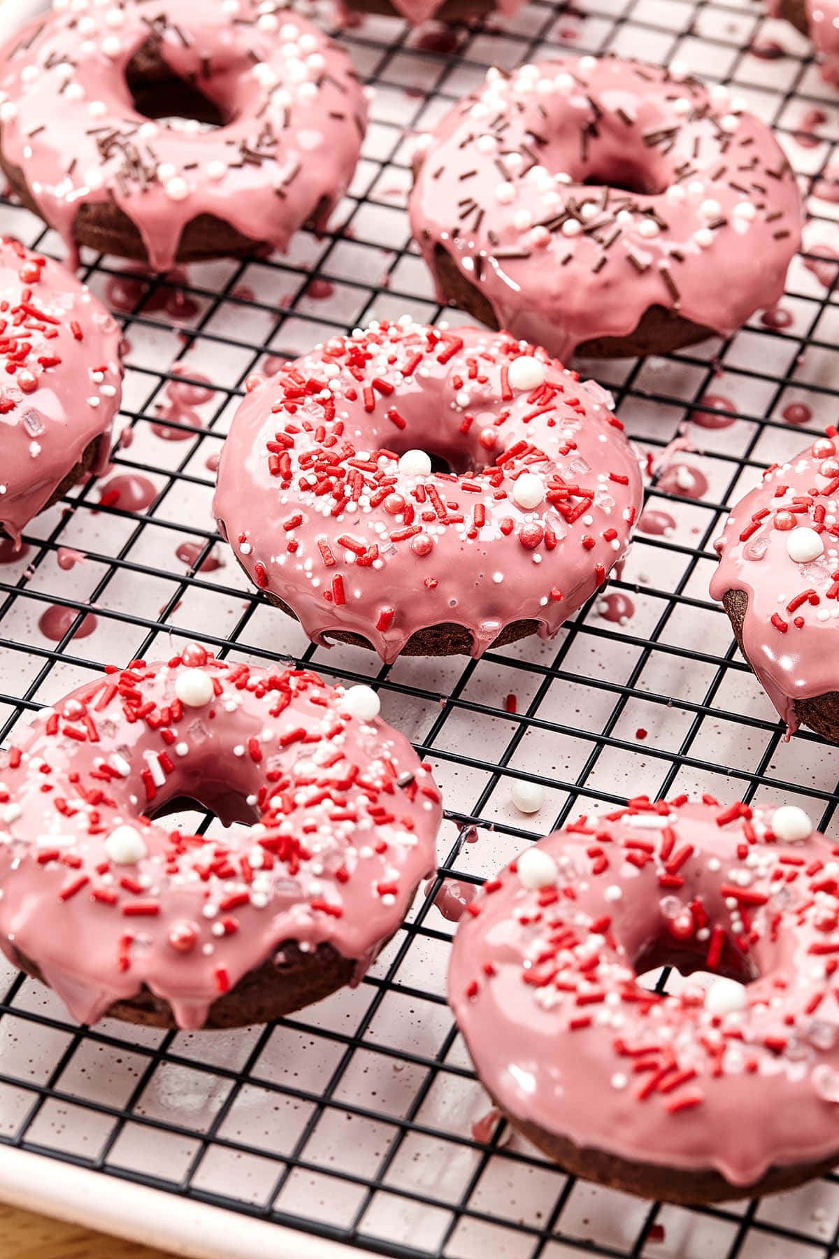 Glazed Donut 桌布 壁紙 — 新鮮的粉紅色巧克力甜甜圈，上面撒有紅色、白色和巧克力糖粒，在黑色金屬架上冷卻。