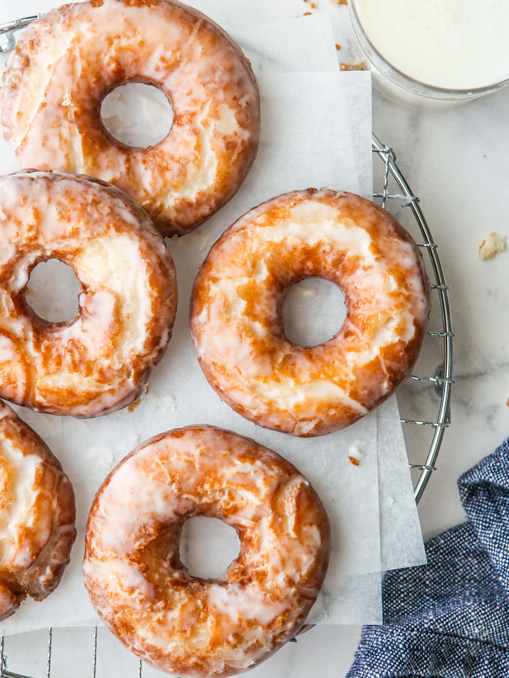 Glazed Donut 桌布 壁紙 — 新鮮的糖霜甜甜圈，金黃色的外皮，放在金屬架上，旁邊有一杯牛奶和藍色布。