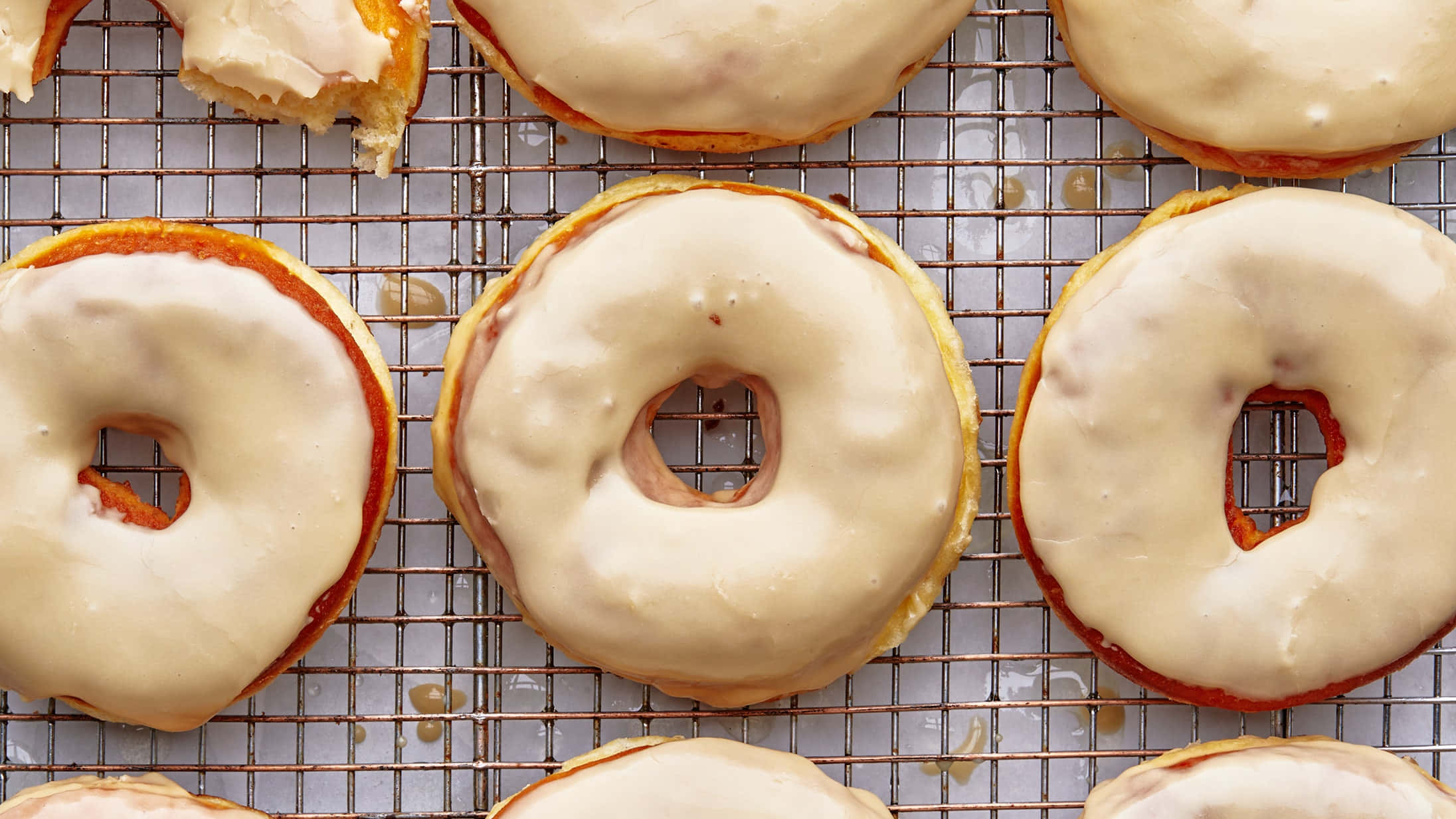 Glazed Donut 桌布 壁紙 — 新鮮的糖霜甜甜圈在金屬架上冷卻，帶有光澤的糖衣和金黃色的邊緣。