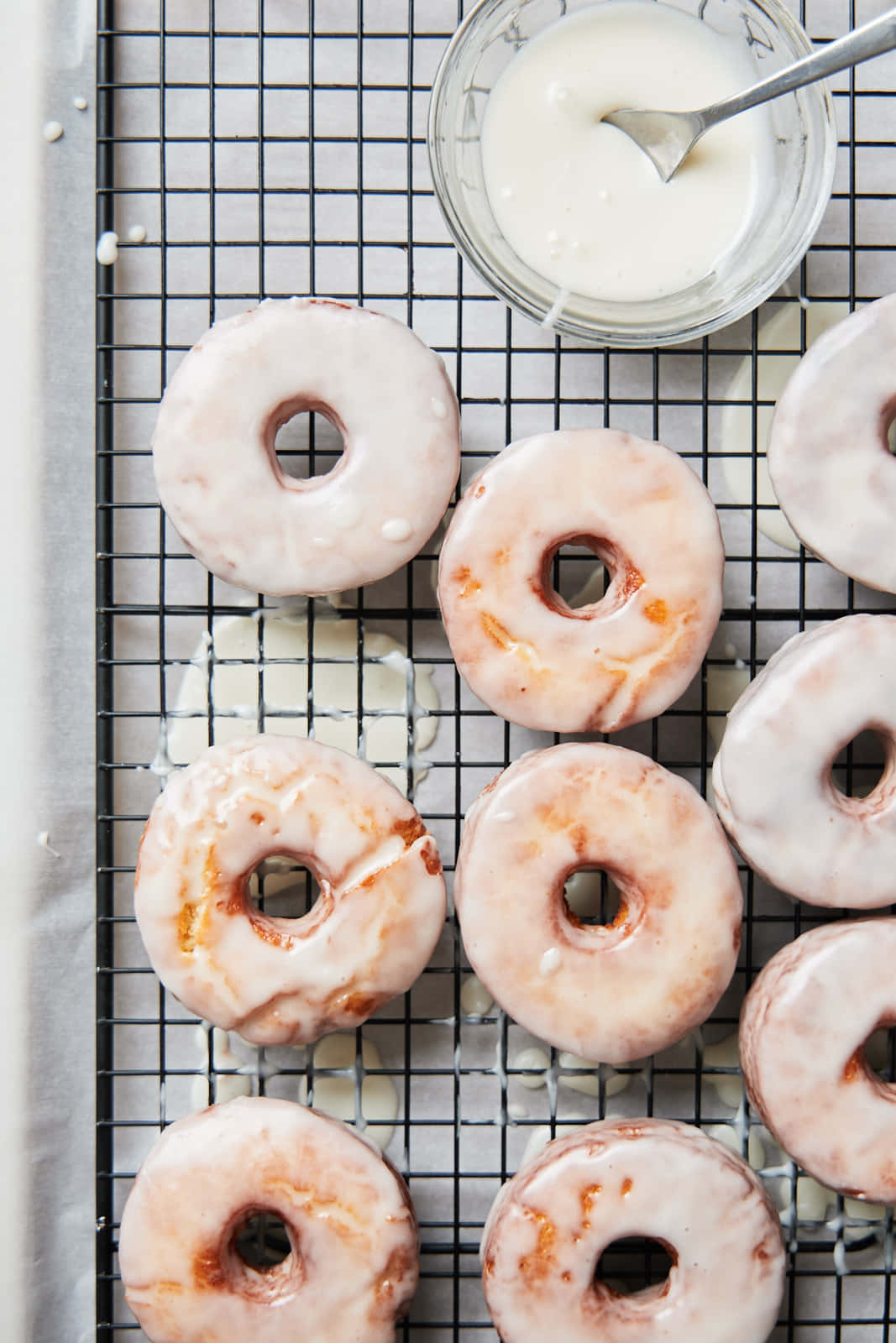Glazed Donut 桌布 壁紙 — 新鮮的糖霜甜甜圈放在黑色金屬架上，旁邊有一碗白色糖霜和一個湯匙。