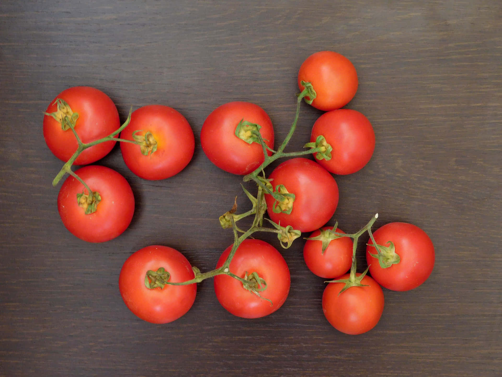 Tomatoes 壁紙 — 新鮮的紅色櫻桃番茄仍掛在綠色藤蔓上，放置在深色木質表面上。