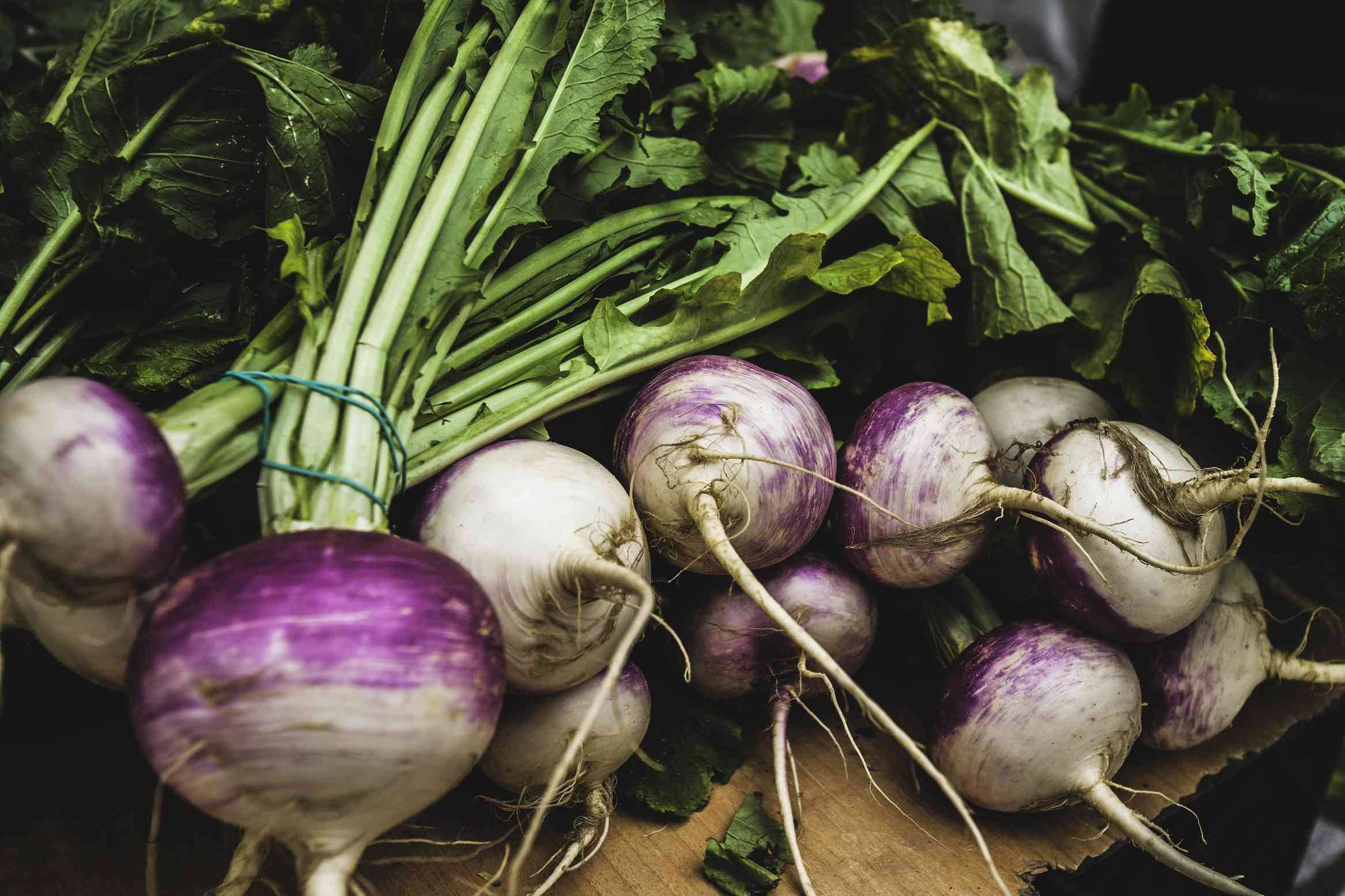 Healthy Food 桌布 壁紙 — 新鮮的紫色和白色蘿蔔，帶有綠色莖部，堆疊在木質表面上。