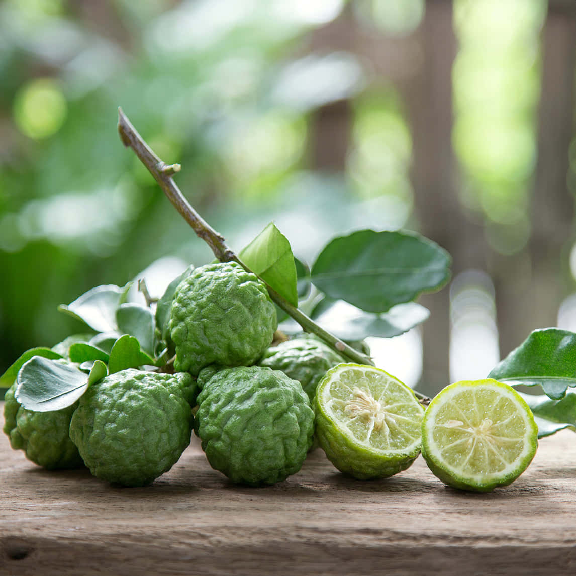 Lime 桌布 壁紙 — 新鮮的綠色柑橘類水果，表皮凹凸不平，切片半個，放在鄉村風格的木質表面上，背景是模糊的樹葉。