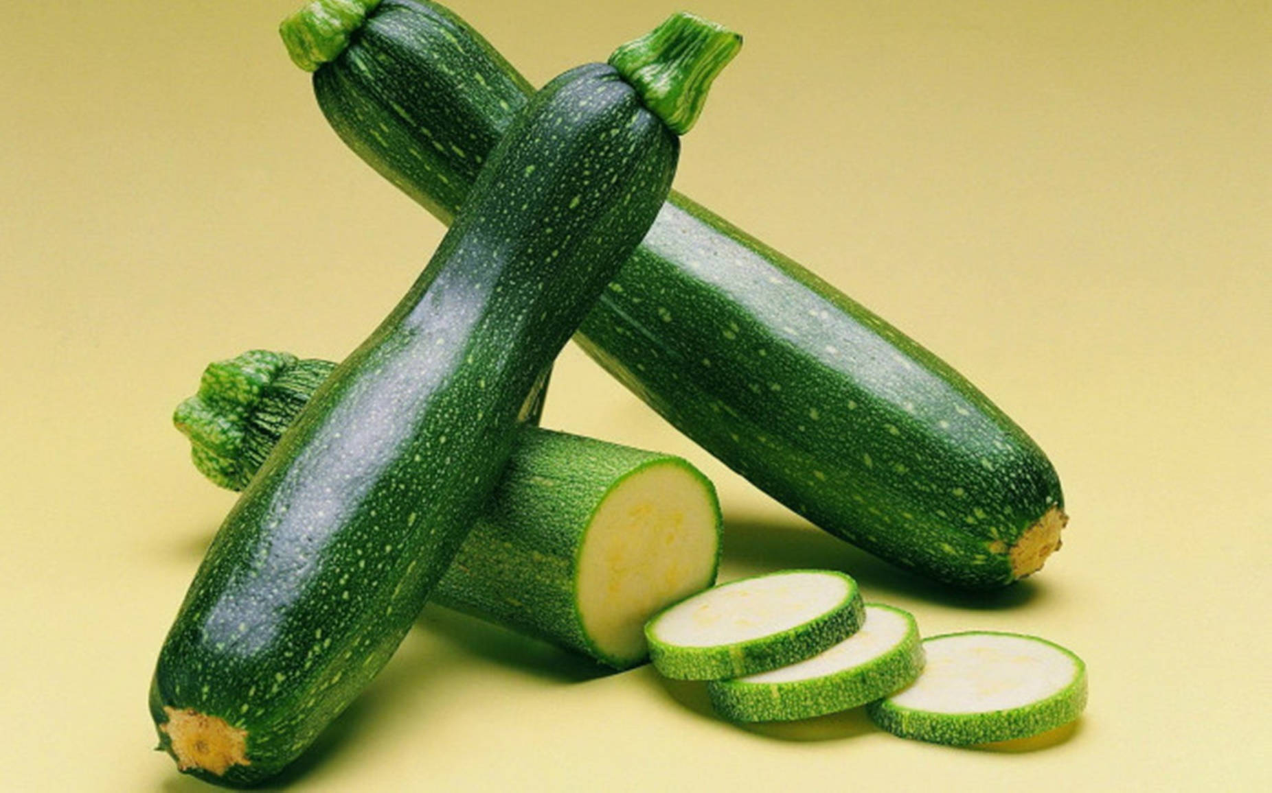 Zucchini 桌布 壁紙 — 新鮮的綠色櫛瓜，帶有斑點皮和切片圓塊，放在溫暖的黃色背景上。
