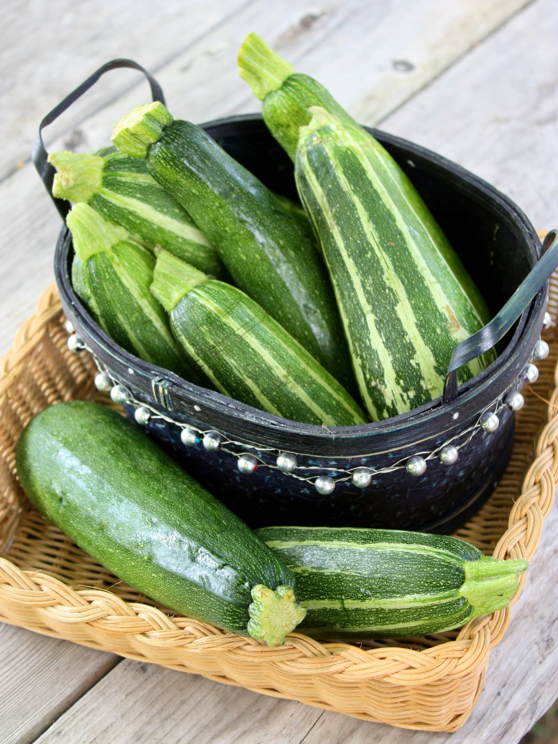Fruits And Vegetables 桌布 壁紙 — 新鮮的綠色櫛瓜帶有淺色條紋，放在一個飾有銀色珠子的黑色金屬桶中，擱在一個編織籃子上，籃子下方是風化的木板。