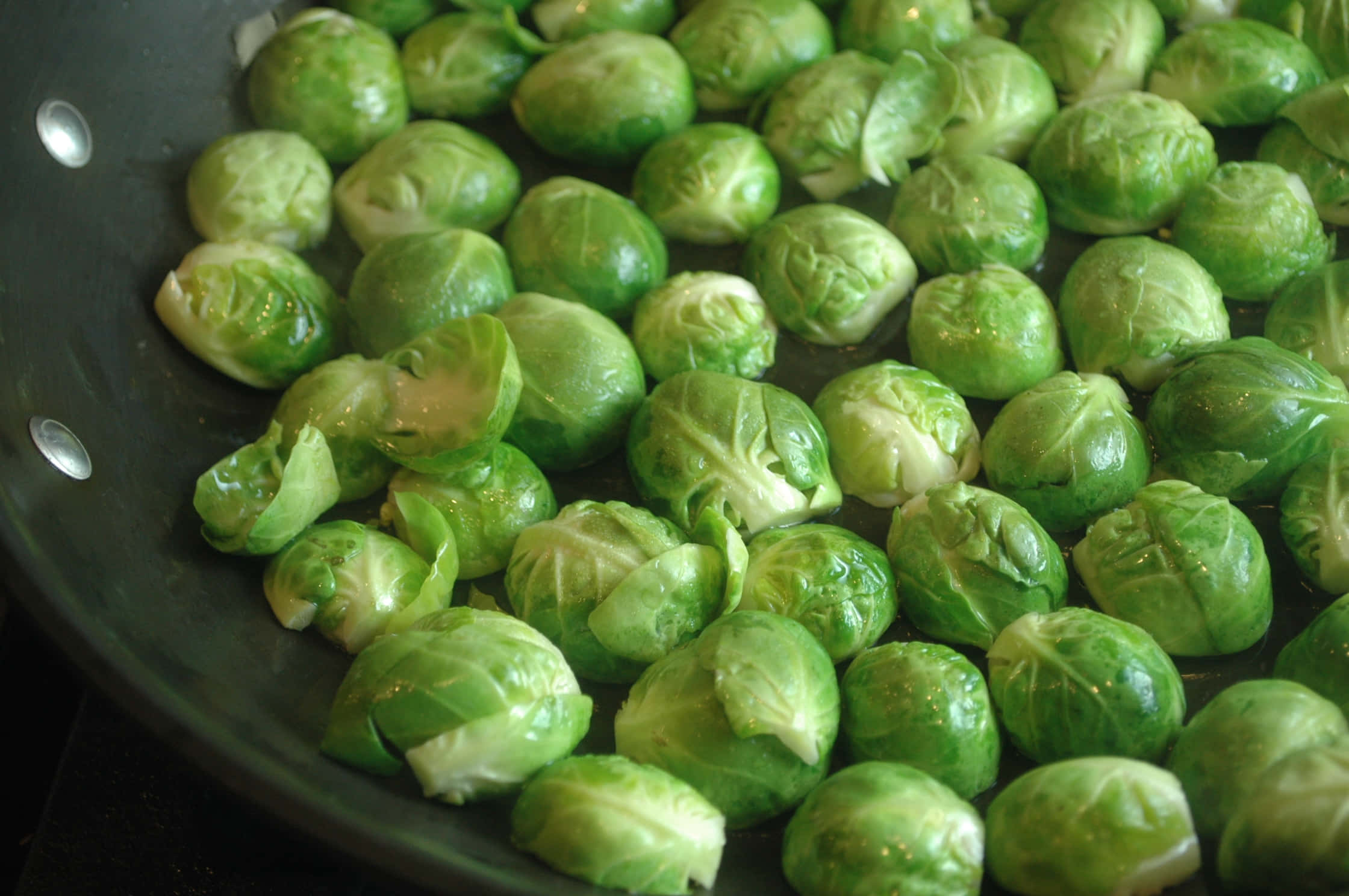 Brussel Sprout 桌布 壁紙 — 新鮮的綠色球芽甘藍在黑色的煎鍋中滋滋作響，油光閃閃，嫩葉上冒出蒸氣。