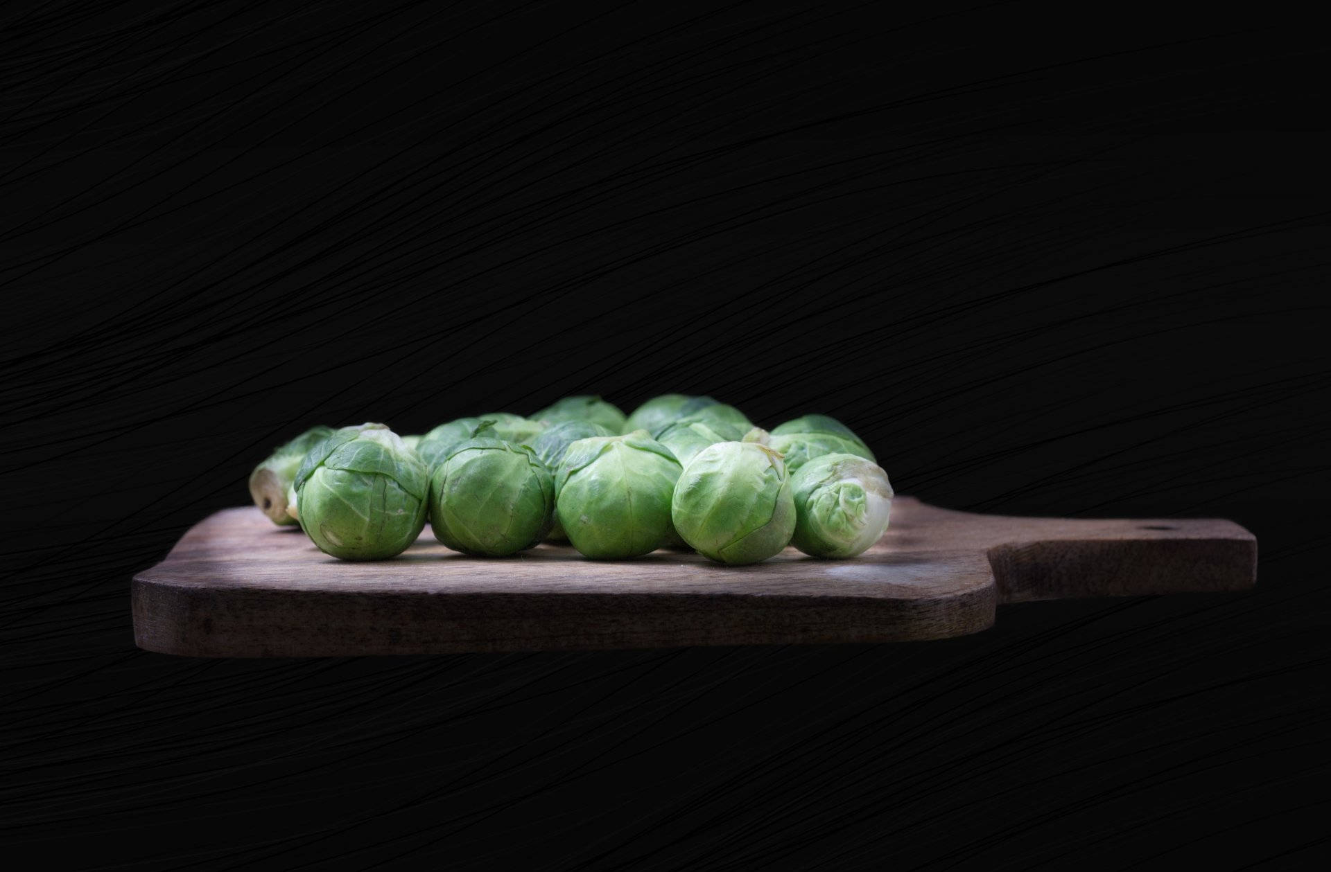 Food Photography 桌布 壁紙 — 新鮮的綠色球芽甘藍整齊地排列在一個質樸的木製砧板上，背景是深色有紋理的。