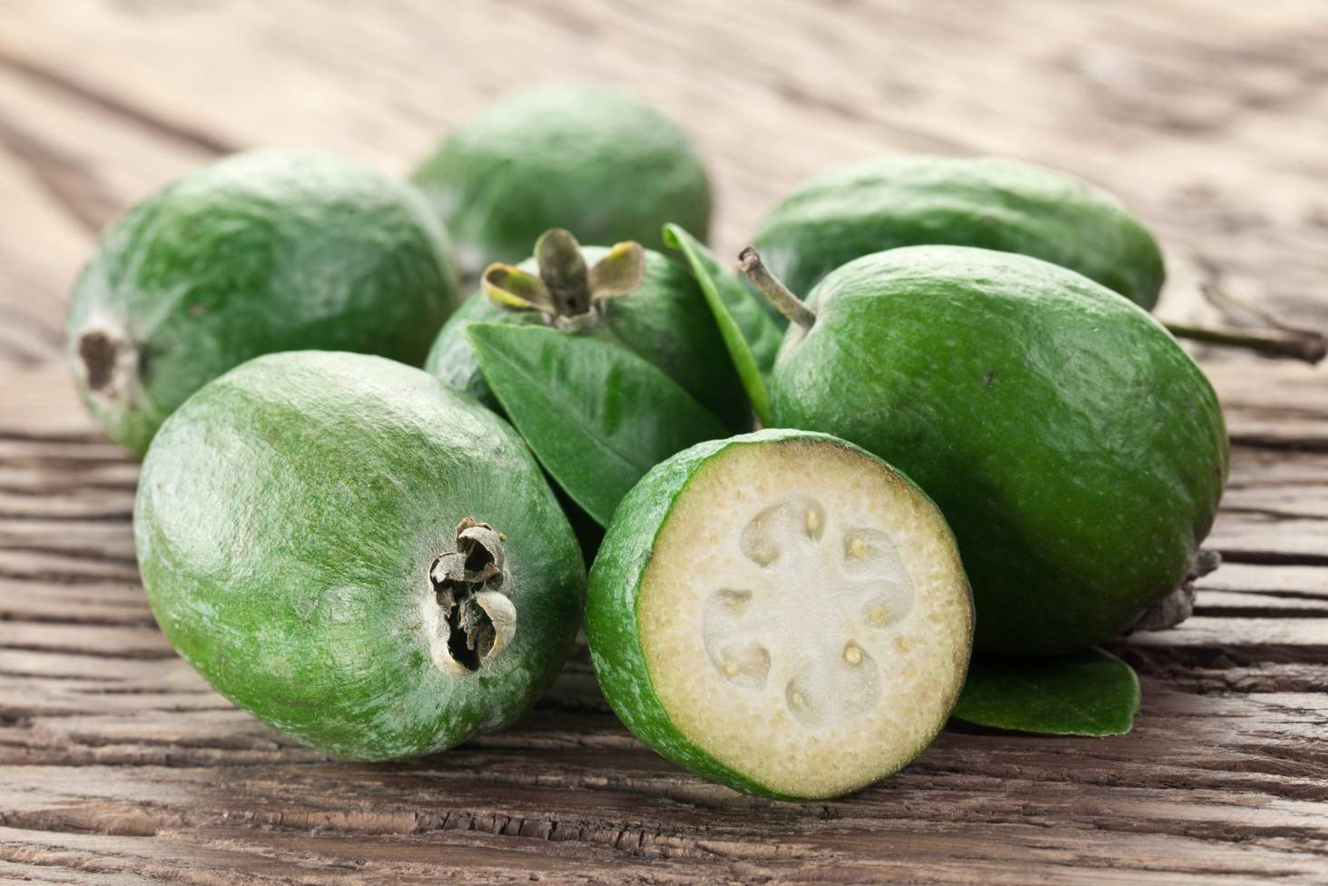 Fruit 桌布 壁紙 — 新鮮的綠色菲油果，其中一個切開，露出白色果肉和種子，放在質樸的木質表面上。