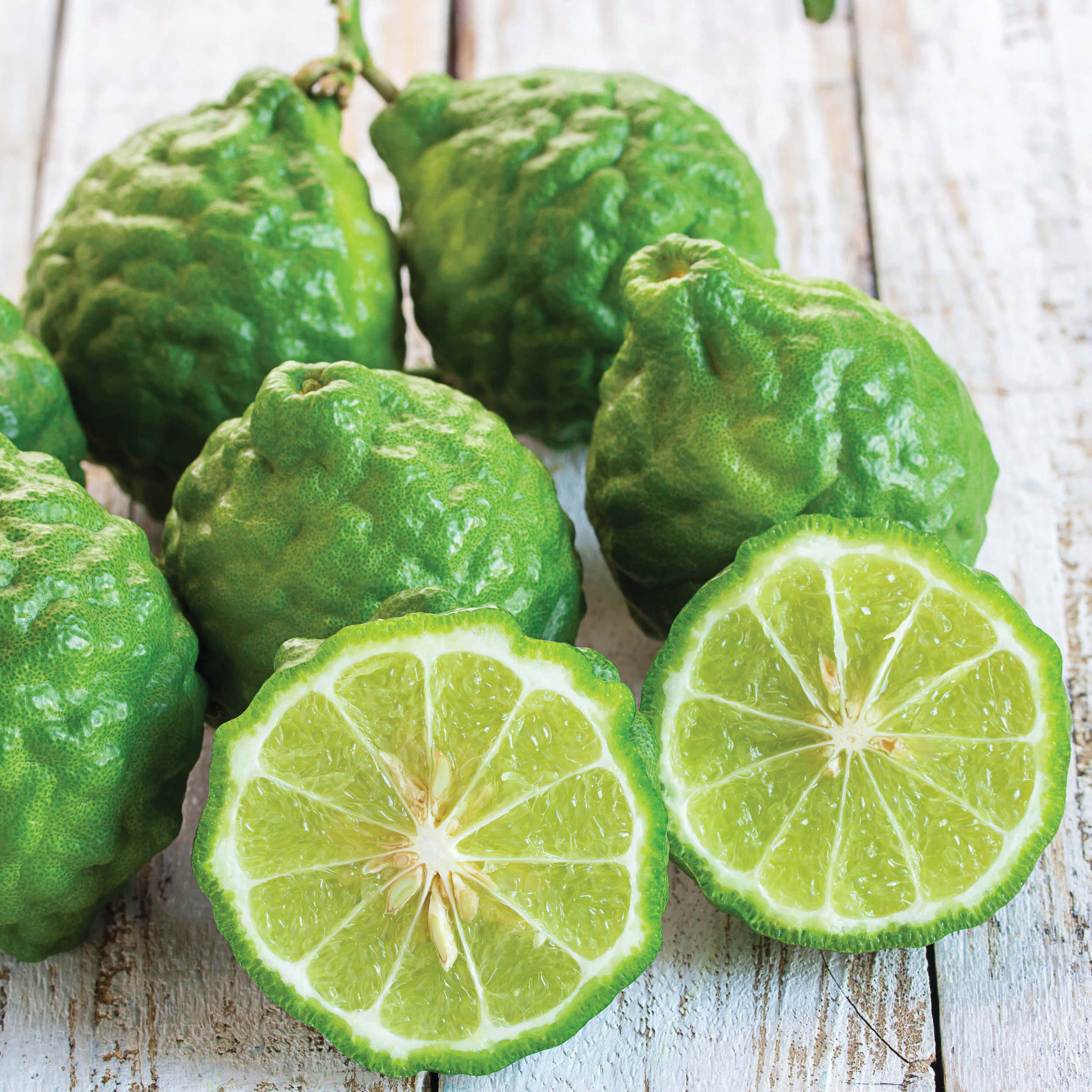 citrus 桌布 壁紙 — 新鮮的綠色萊姆，表皮凹凸不平，多汁的分瓣半邊，放在一塊經風化的白色木質表面上。