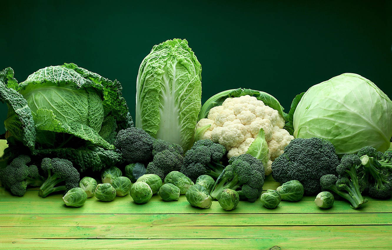 Broccoli 桌布 壁紙 — 新鮮的綠色蔬菜，包括高麗菜、青花菜和花椰菜，排列在充滿活力的綠色木質表面上，背景為深綠色。