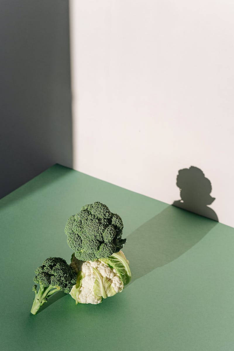 Vegetables 桌布 壁紙 — 新鮮的綠花椰菜和白花椰菜放在綠色表面上，在明亮光線下於白色牆壁上投射出銳利的陰影。