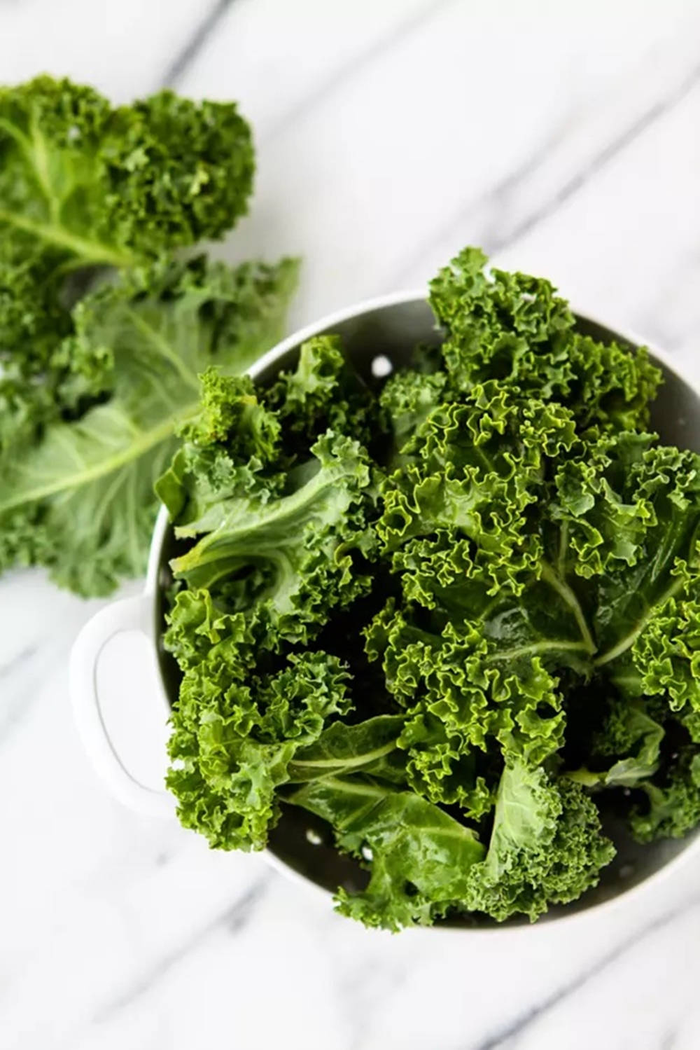 Vegetable 桌布 壁紙 — 新鮮的羽衣甘藍葉填滿白色濾鍋，置於大理石檯面上，柔和自然光線照射。