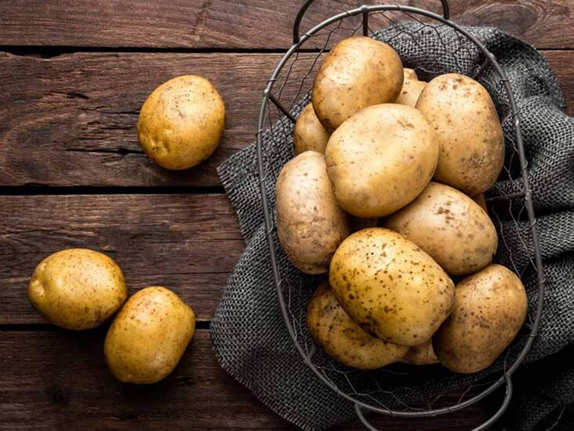 Potato 桌布 壁紙 — 新鮮的鄉村馬鈴薯放在鐵絲籃中，置於鋪有灰色布的深色木桌上。