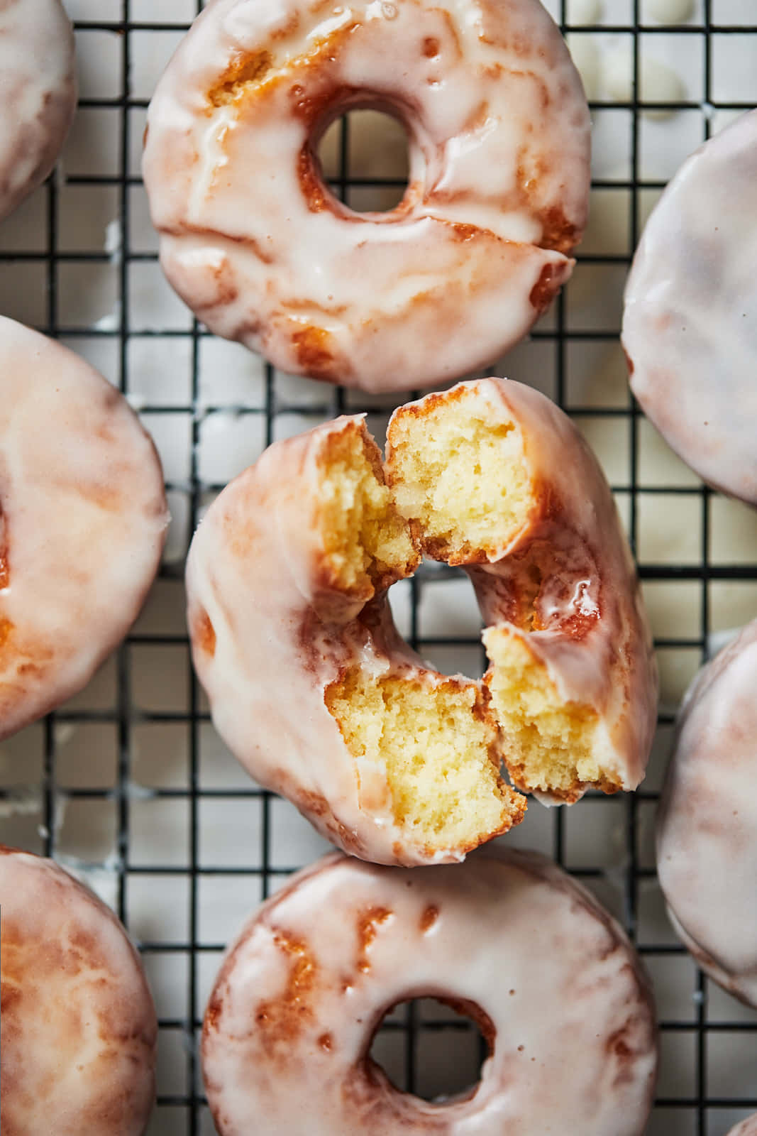 Glazed Donut 桌布 壁紙 — 新鮮的釉面甜甜圈，其中一個被咬開，放在冷卻架上，露出柔軟的金色麵包屑。