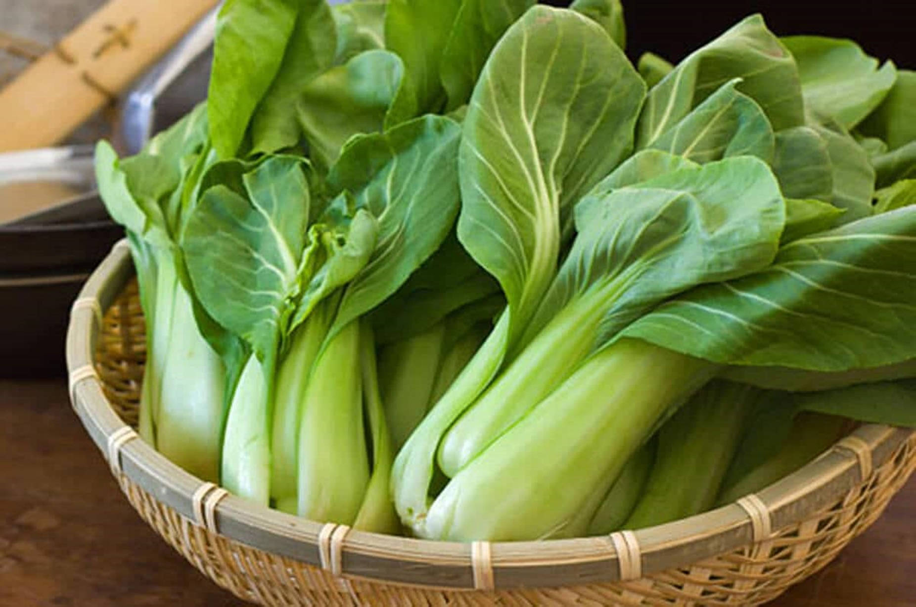 Vegetables 桌布 壁紙 — 新鮮的青江菜，翠綠的葉片和淺色的莖，裝滿了一個放在木質表面的竹編籃子。