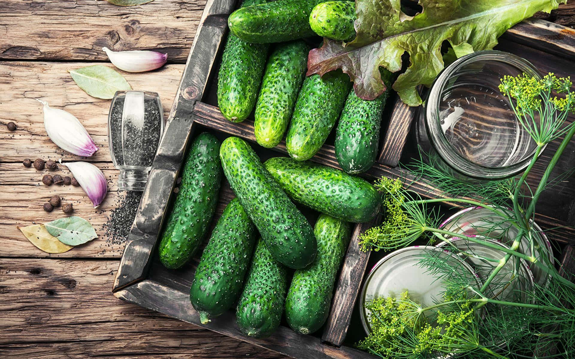 cucumber 桌布 壁紙 — 新鮮的青瓜在質樸的木箱中閃爍著水珠，旁邊有香草、大蒜和香料，放在風化的木頭上。