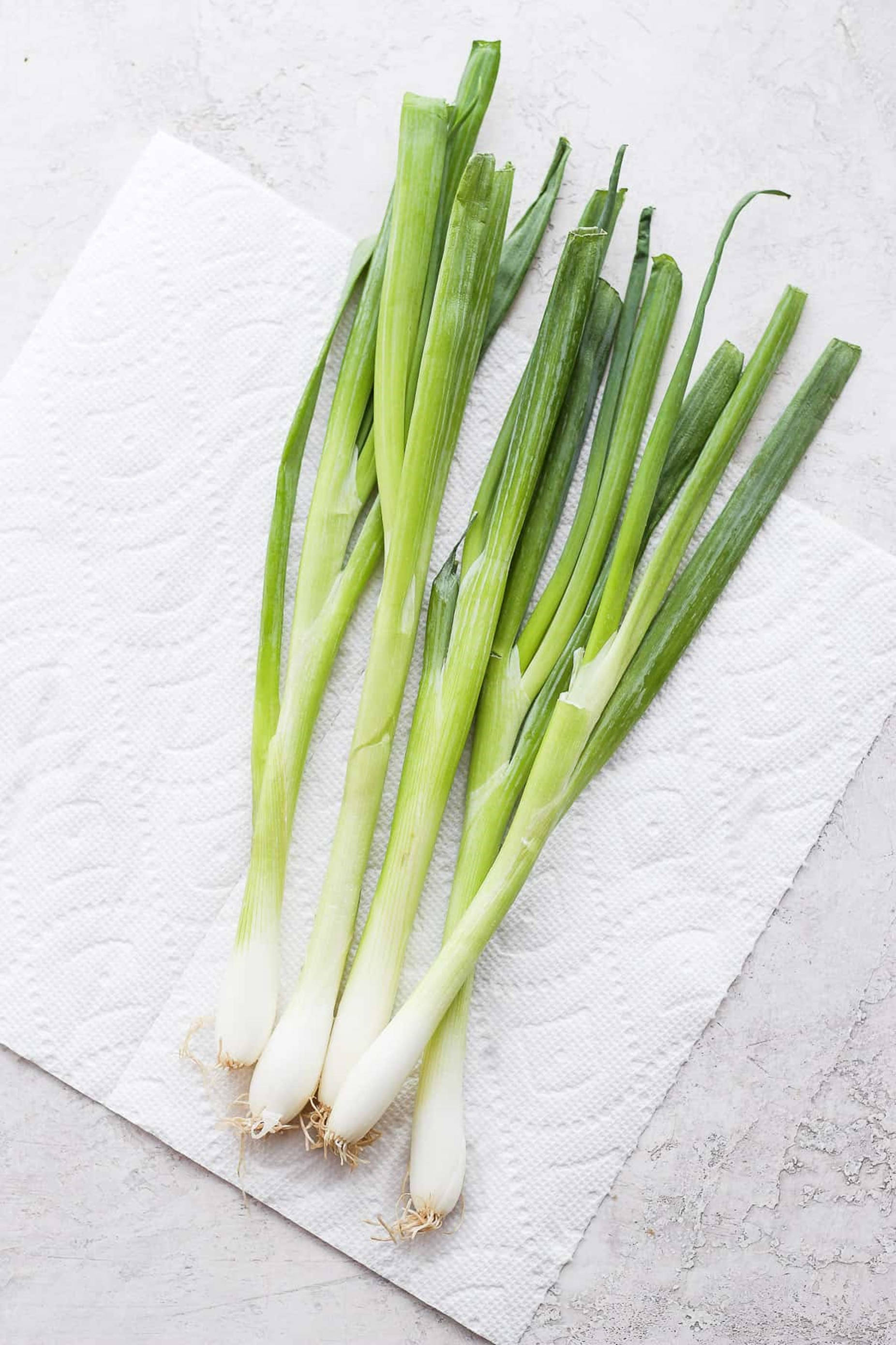 food iPhone 桌布 壁紙 — 新鮮的青蔥帶白色蔥頭，放在有紋理的白色紙巾上，背景為淺灰色表面。