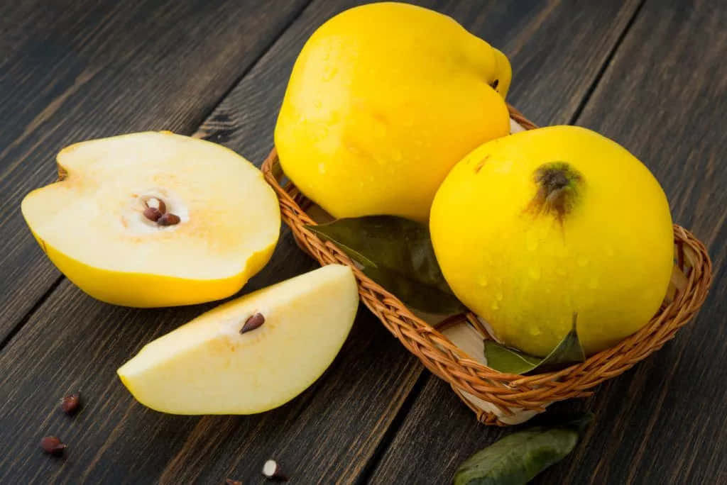 Quince 桌布 壁紙 — 新鮮的黃色榲桲帶有露珠，放在深色木桌上的編織籃中，其中一個切開露出淡色果肉和深色種子。