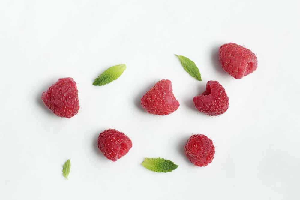 Raspberry 桌布 壁紙 — 新鮮紅覆盆子和綠色薄荷葉散落在潔白表面上。