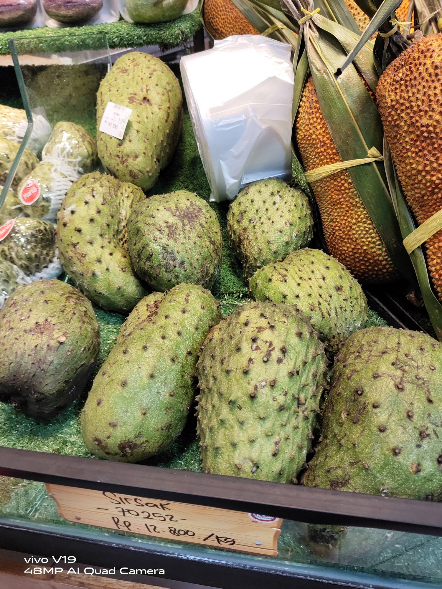 Fruits 桌布 壁紙 — 新鮮綠色刺果番荔枝（帶刺表皮）與菠蘿蜜一同陳列在市場攤位的仿真草皮上。