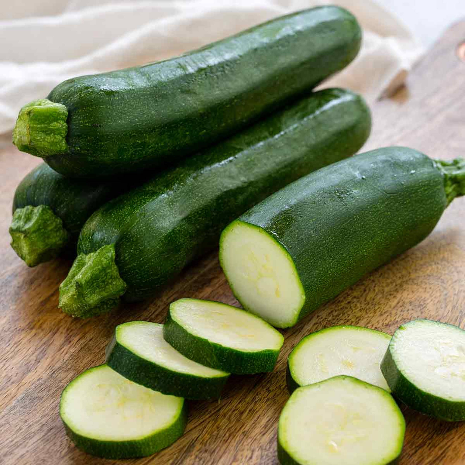 Vegetables 桌布 壁紙 — 新鮮綠色櫛瓜（完整及切片）放在溫暖的木砧板上，背景為柔軟布料。