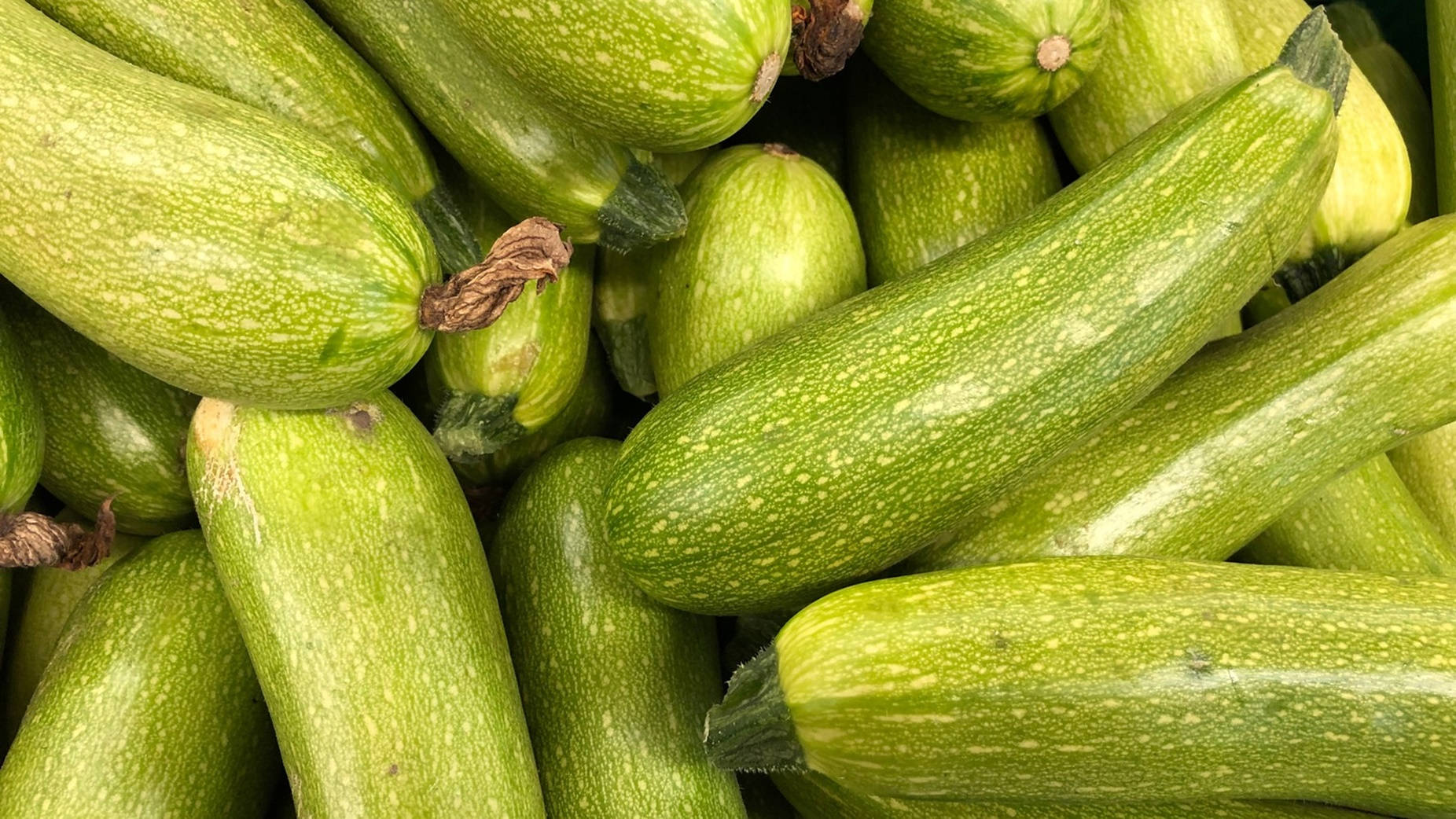 Vegetables 桌布 壁紙 — 新鮮綠色櫛瓜堆疊在一起的近距離照片，顯示出紋理表皮和乾燥的莖。