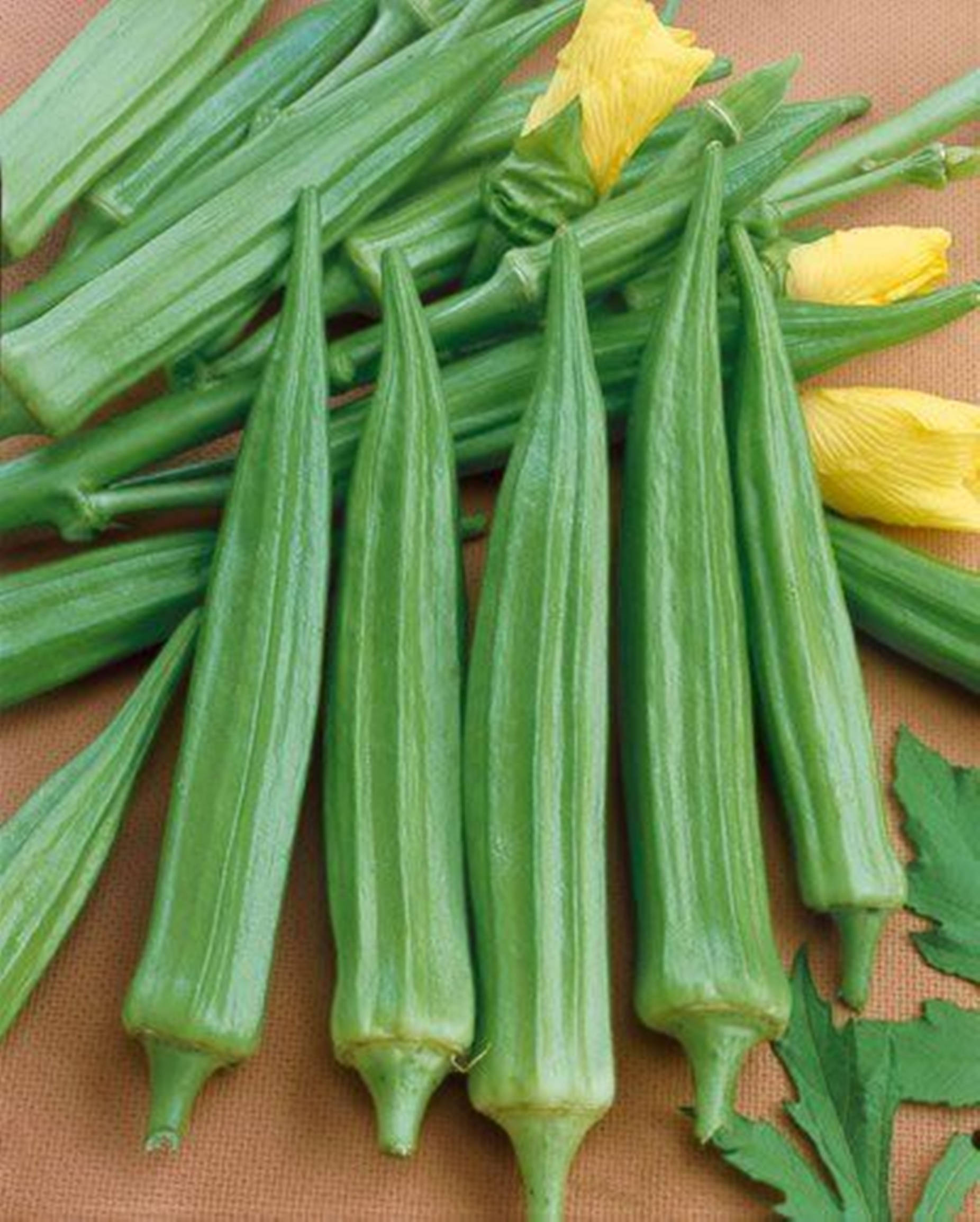 Healthy Food 桌布 壁紙 — 新鮮綠色秋葵莢與黃色花朵排列在帶紋理的棕色表面上。