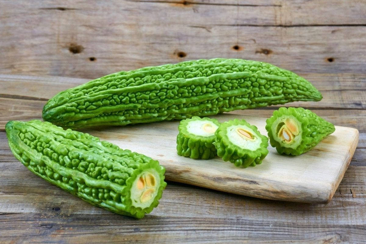sliced 桌布 壁紙 — 新鮮綠色苦瓜，表面凹凸不平，切片後露出淡色內籽，放在鄉村風木砧板上。