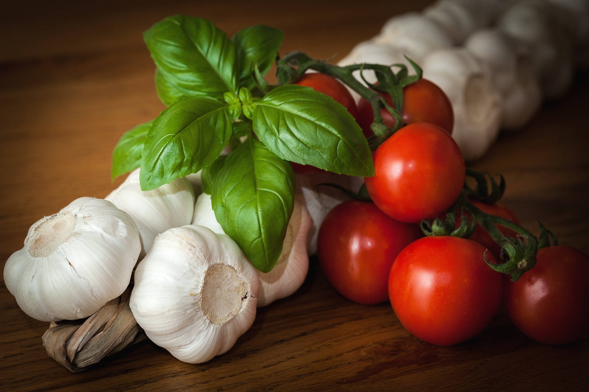 Vegetable 桌布 壁紙 — 新鮮羅勒、大蒜和櫻桃番茄在溫暖的木質表面上以柔和自然光線排列。