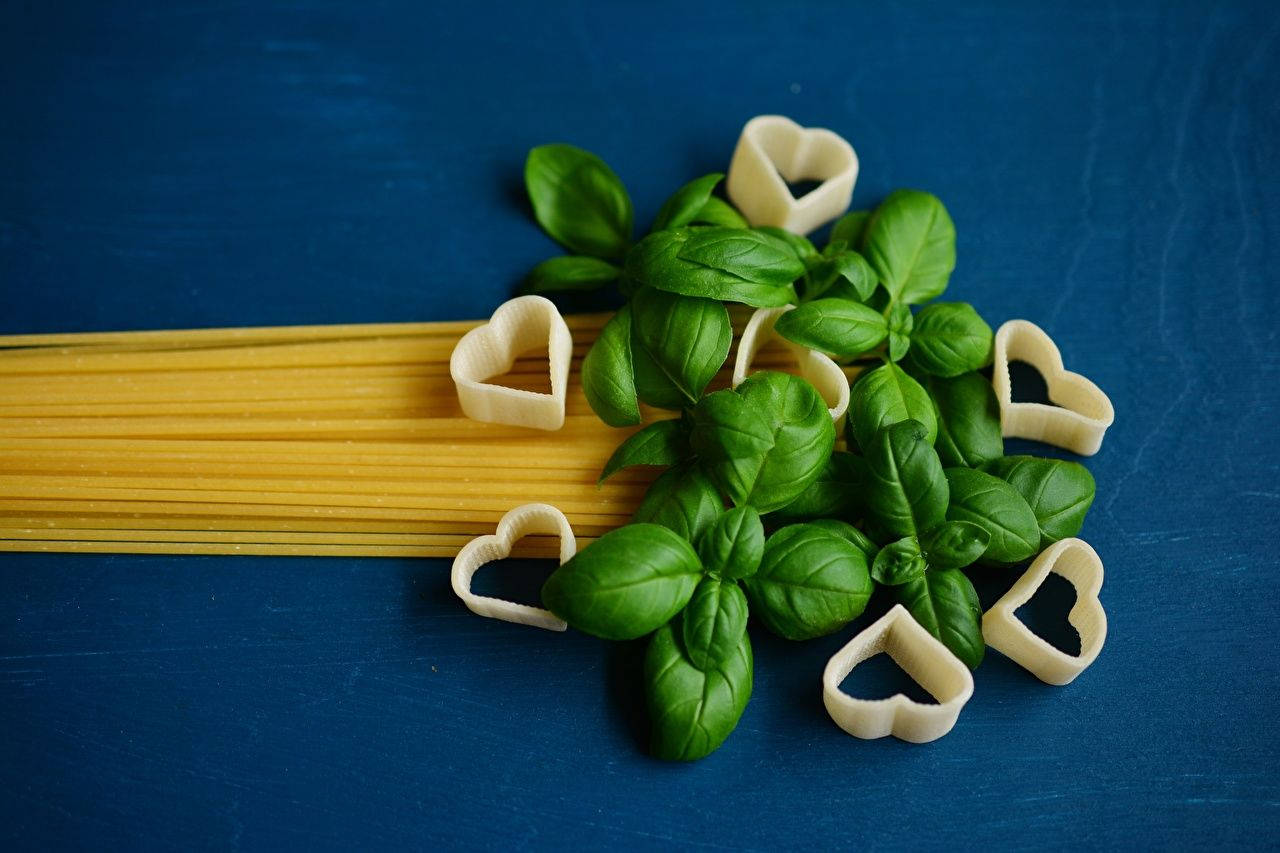 Vegetables 桌布 壁紙 — 新鮮羅勒葉和心形義大利麵依偎在未煮熟的義大利麵旁邊，置於深藍色紋理表面上。