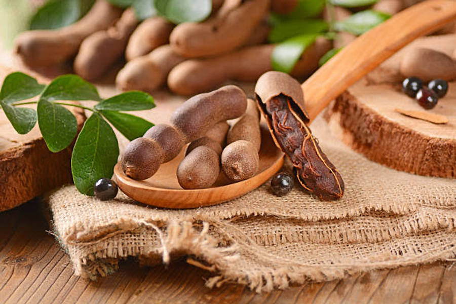 beans 桌布 壁紙 — 新鮮羅望子莢和種子放在木勺上，置於粗麻布和質樸木材之上，周圍環繞著綠葉。