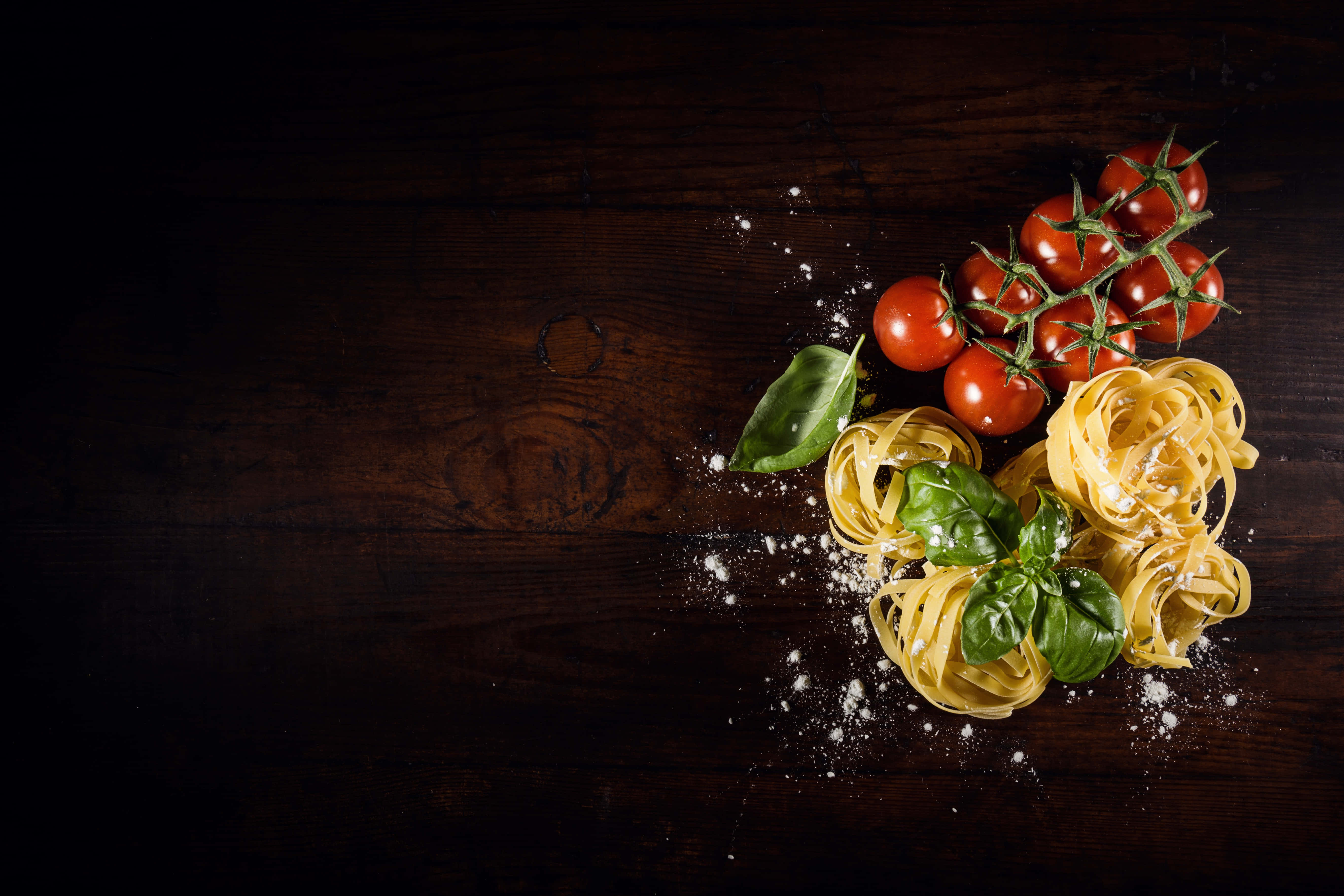 4K Pasta 桌布 壁紙 — 新鮮義大利麵、番茄和羅勒放在深色木質表面上，撒有帕瑪森起司。