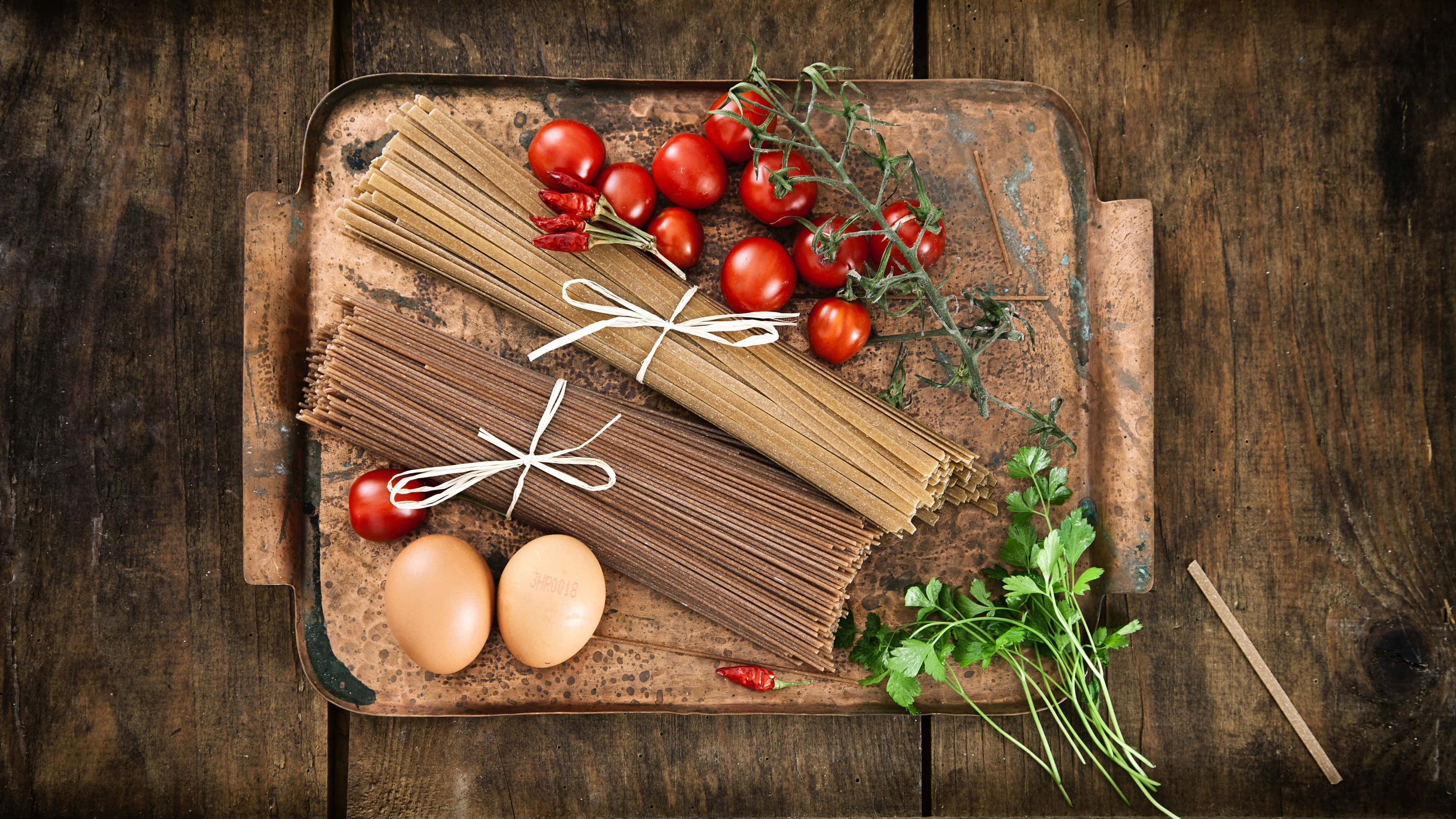 4K Pasta 桌布 壁紙 — 新鮮義大利麵、雞蛋、番茄和香草整齊擺放在一個質樸的金屬托盤上，置於風化木頭之上。