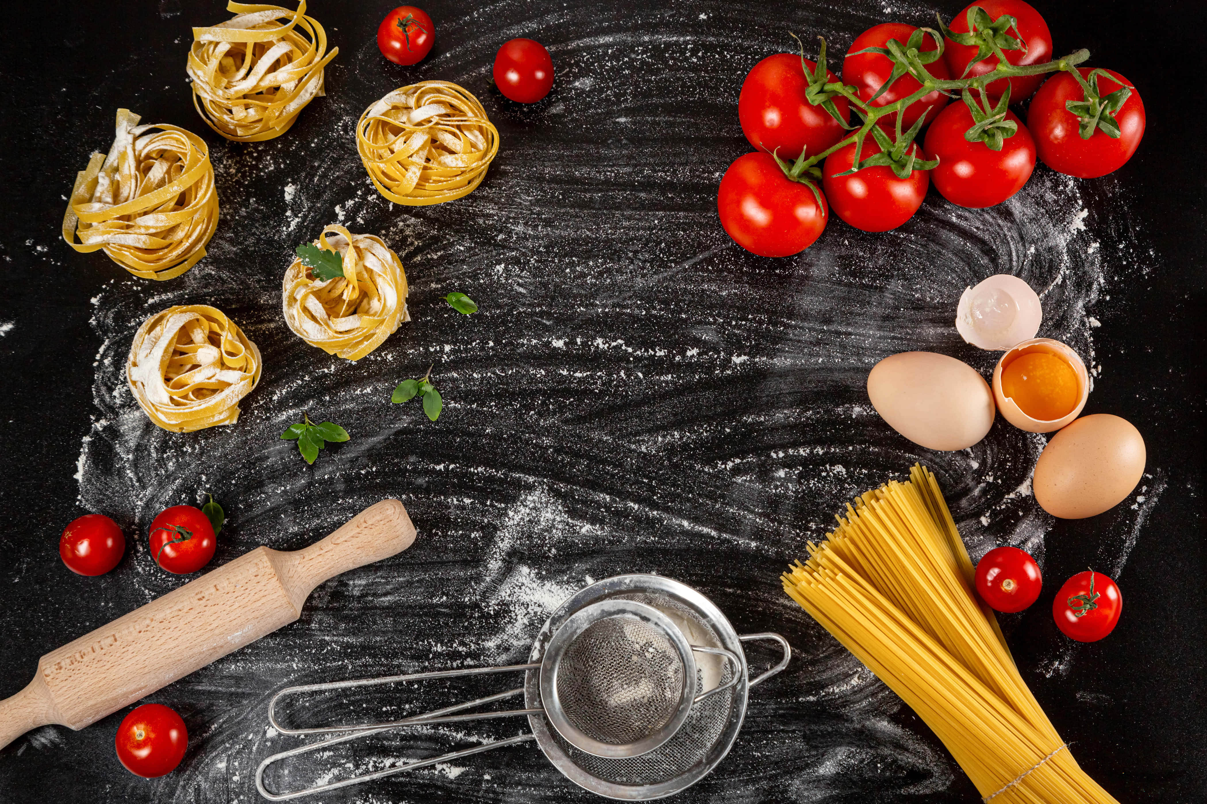 4K Pasta 桌布 壁紙 — 新鮮義大利麵材料如番茄、雞蛋和麵粉，藝術性地排列在深色黑板表面上。