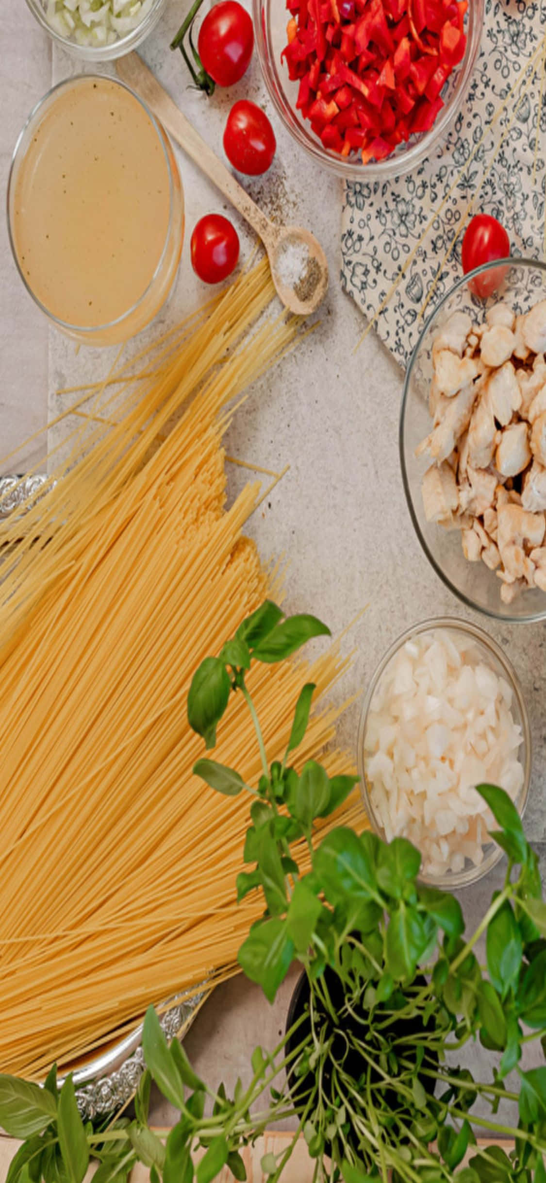 iPhone X Pasta 桌布 壁紙 — 新鮮義大利麵食材如義大利麵、雞肉、番茄和羅勒，整齊擺放在淺色料理檯上備用。