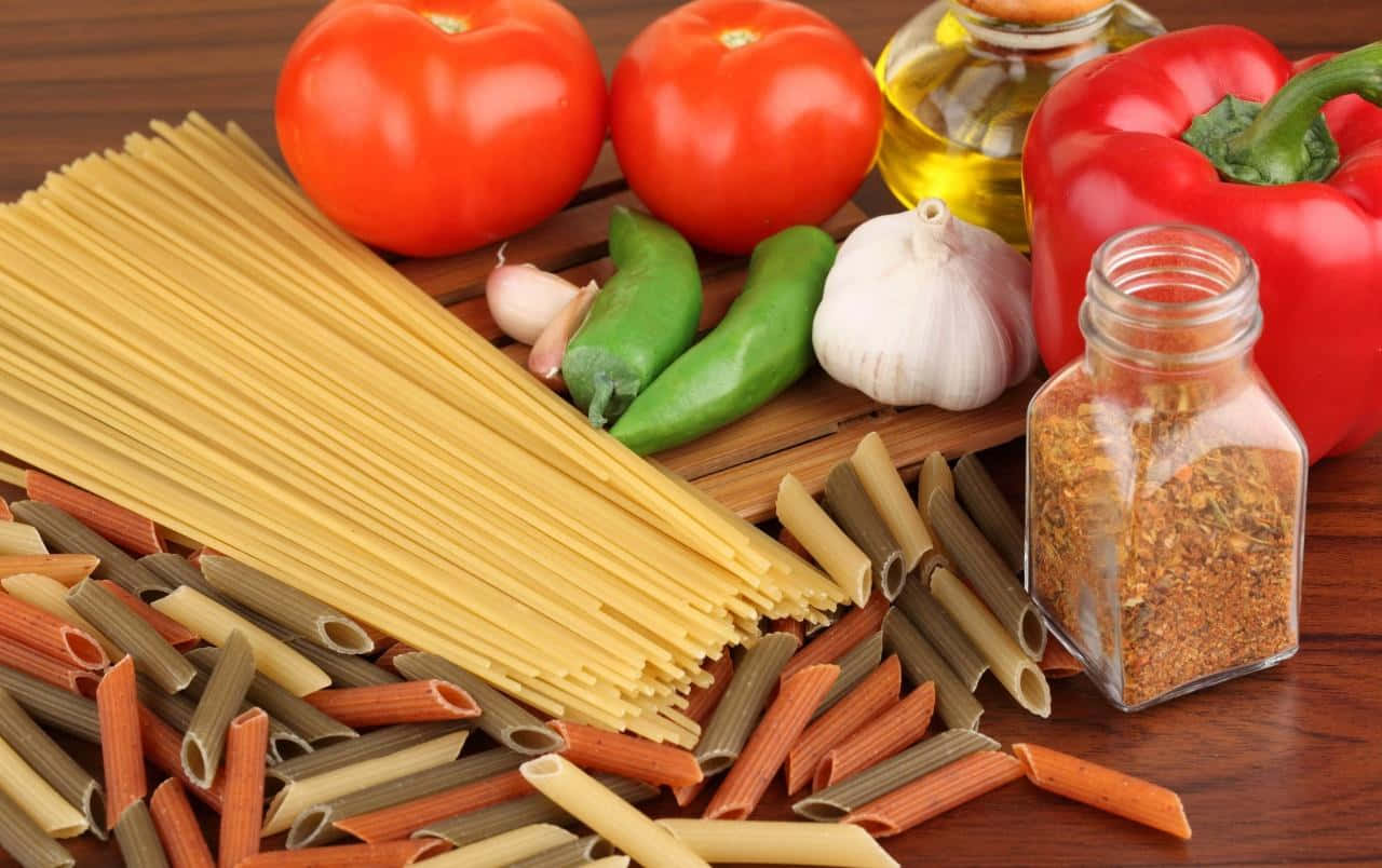 Pasta 桌布 壁紙 — 新鮮義大利麵食材的鮮豔排列，包括番茄、甜椒、大蒜和香料，擺放在木質表面上。